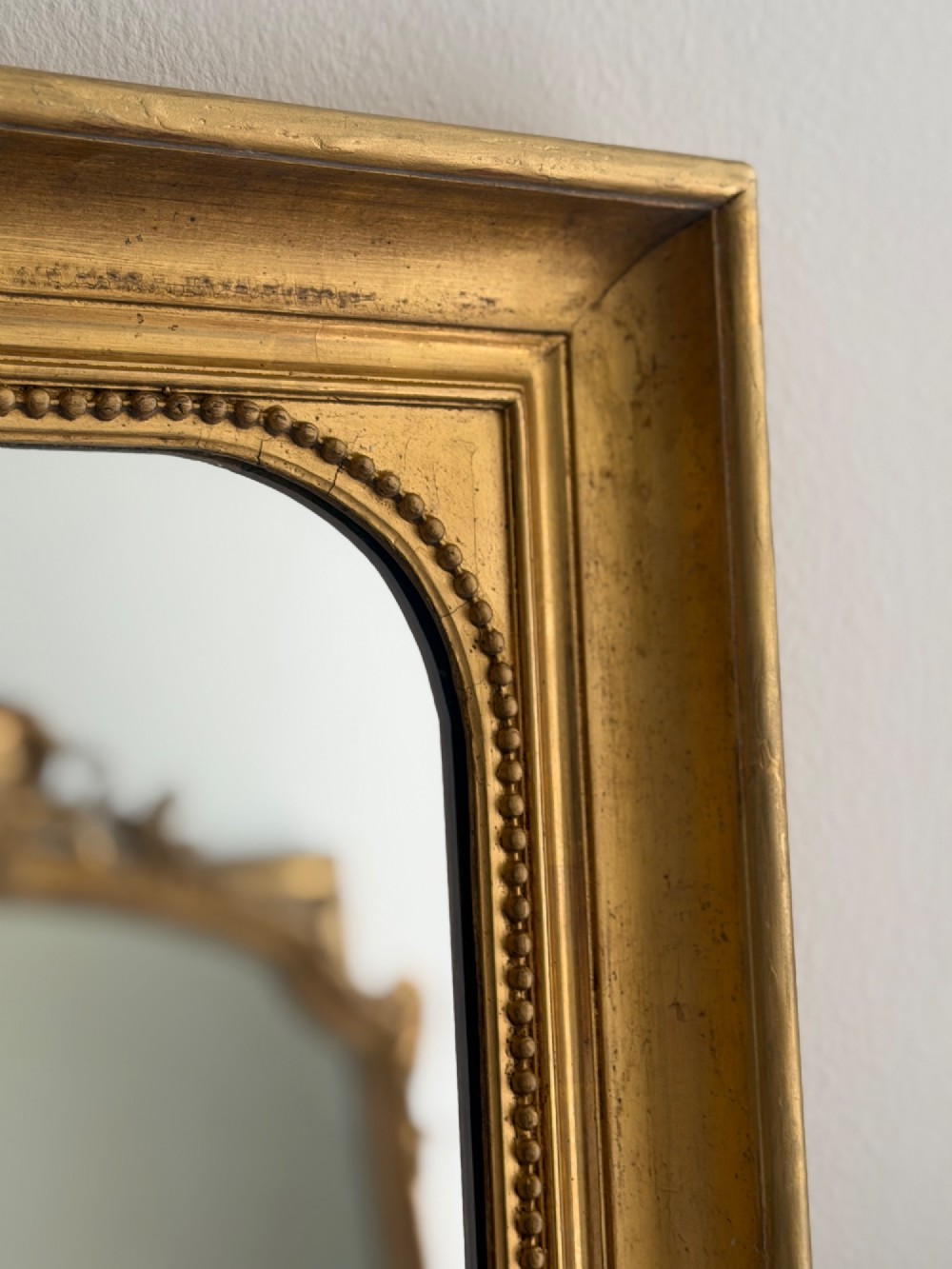 A rectangular antique French wall mirror featuring a gilded wood frame with a beaded inner border. View V