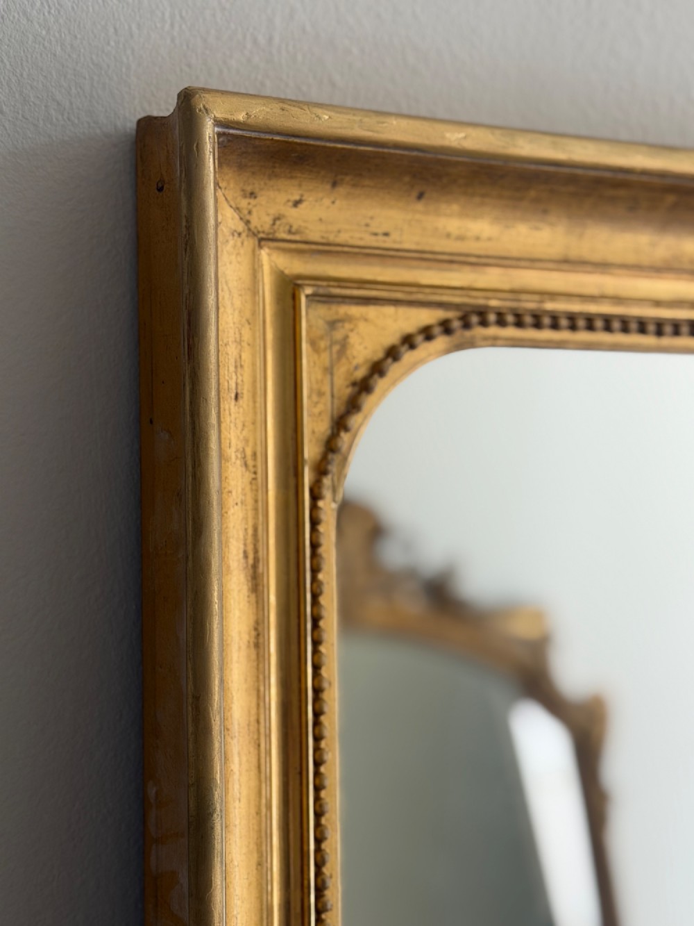 A rectangular antique French wall mirror featuring a gilded wood frame with a beaded inner border. View VI