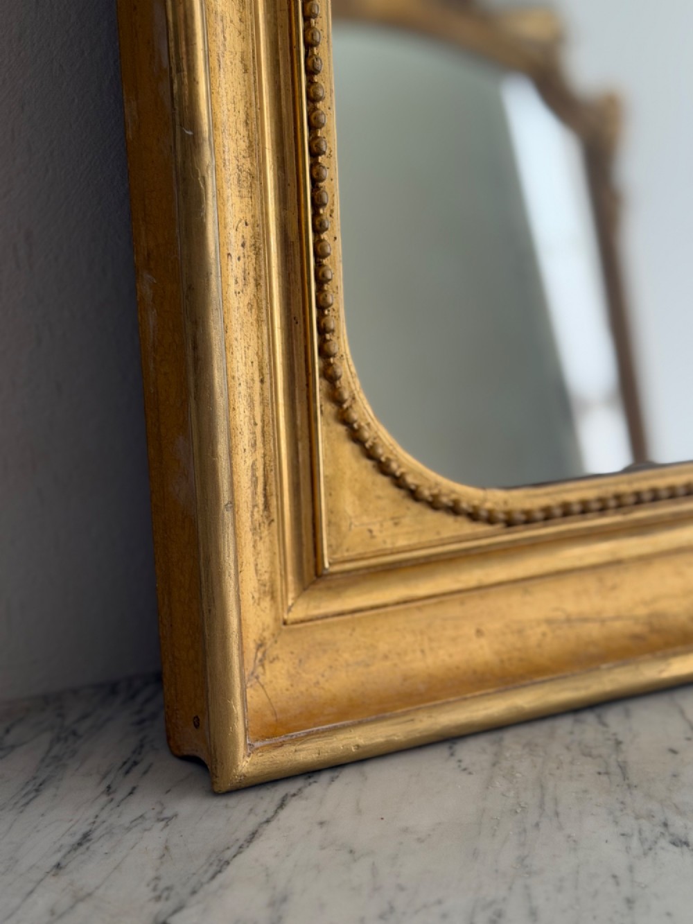 A rectangular antique French wall mirror featuring a gilded wood frame with a beaded inner border. View VII