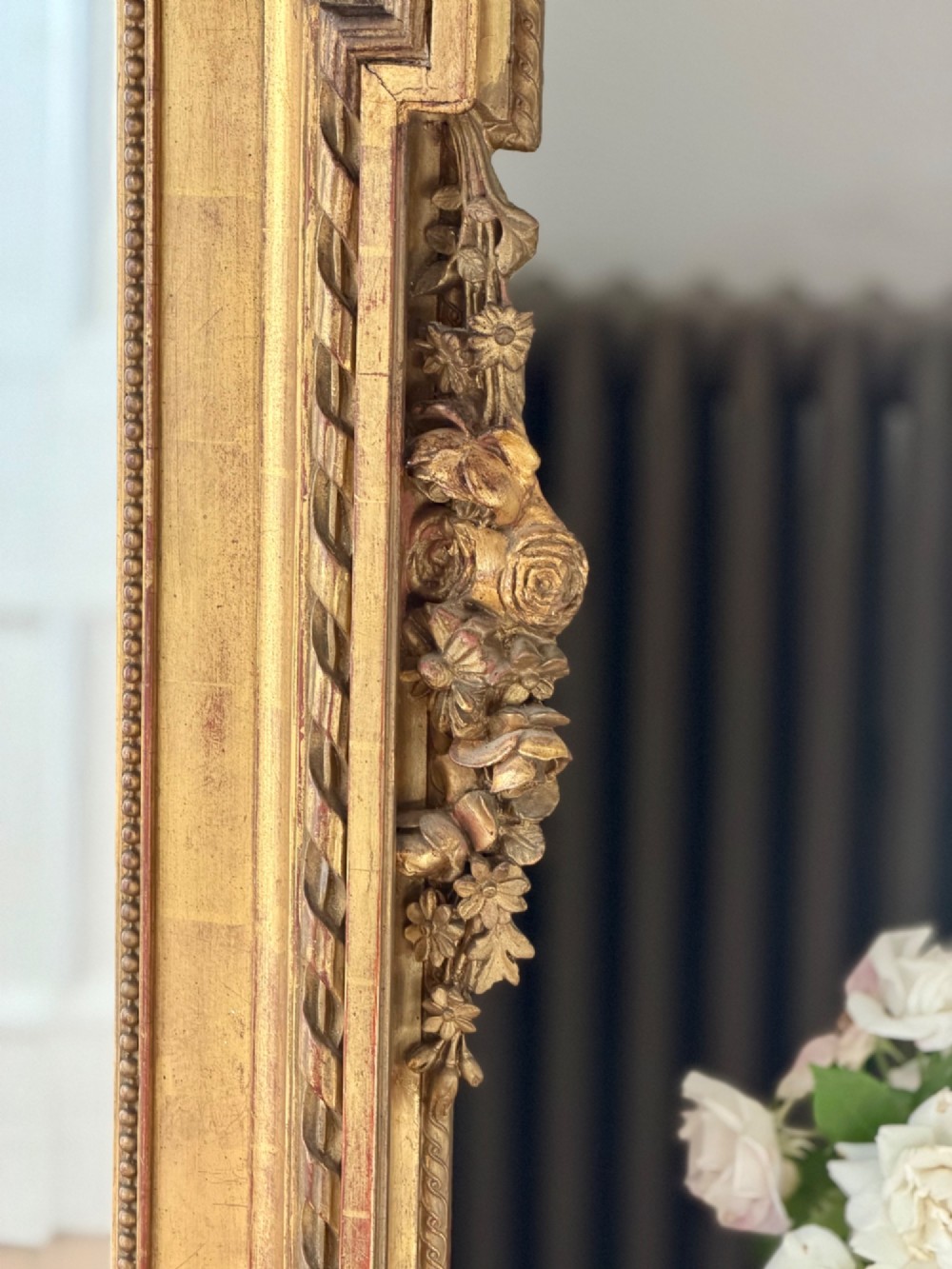 A rectangular French Louis XVI style giltwood mirror featuring a carved ribbon cresting, draped floral swags, and a bevelled glass mirror plate. View III