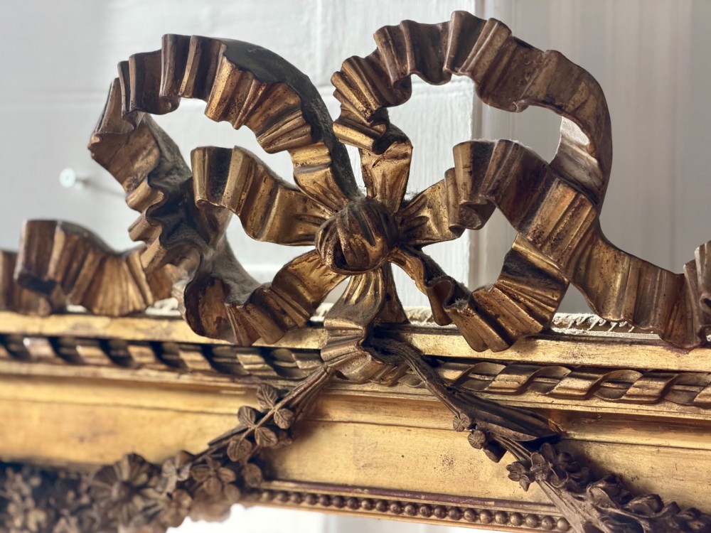 A rectangular French Louis XVI style giltwood mirror featuring a carved ribbon cresting, draped floral swags, and a bevelled glass mirror plate. View IV