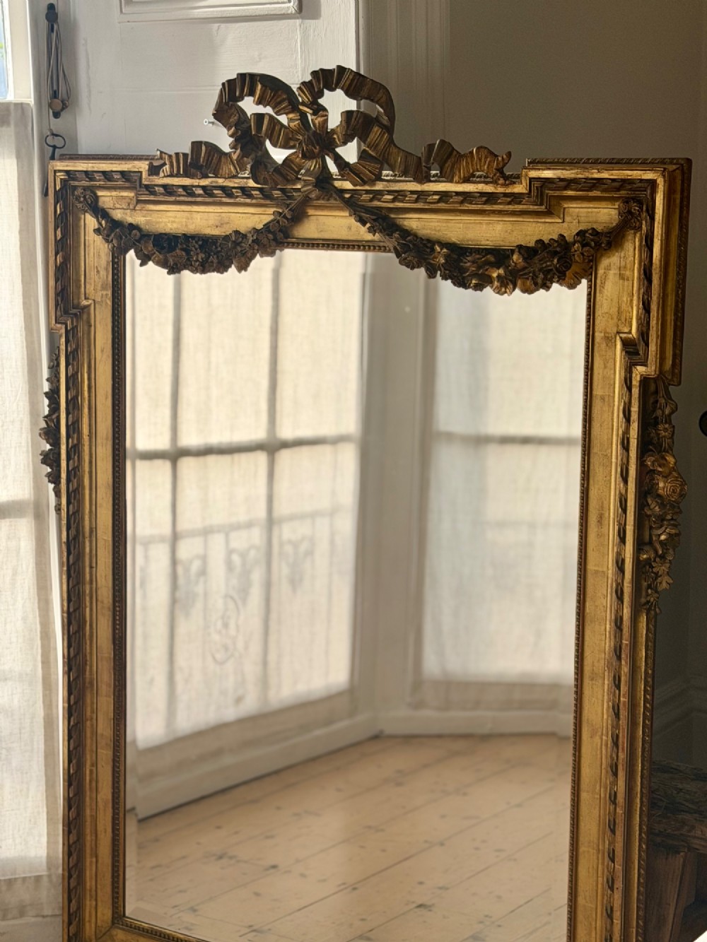 A rectangular French Louis XVI style giltwood mirror featuring a carved ribbon cresting, draped floral swags, and a bevelled glass mirror plate. View VII