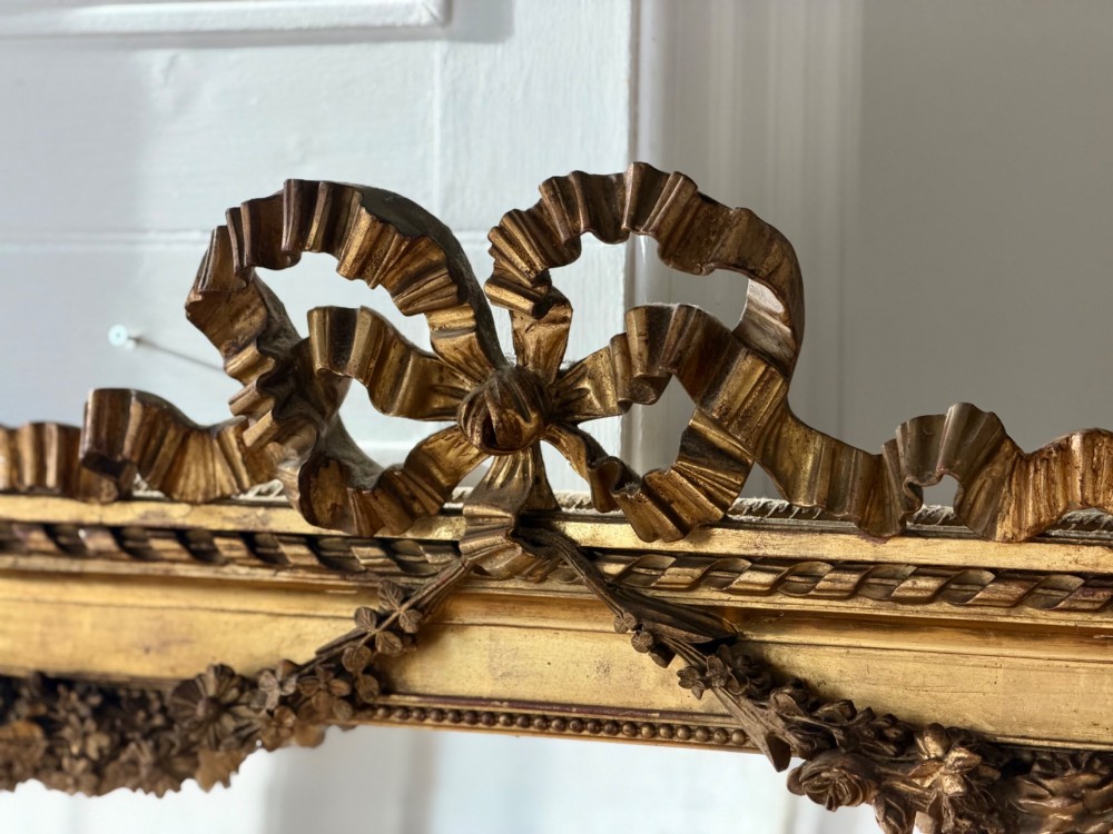 A rectangular French Louis XVI style giltwood mirror featuring a carved ribbon cresting, draped floral swags, and a bevelled glass mirror plate. View VIII