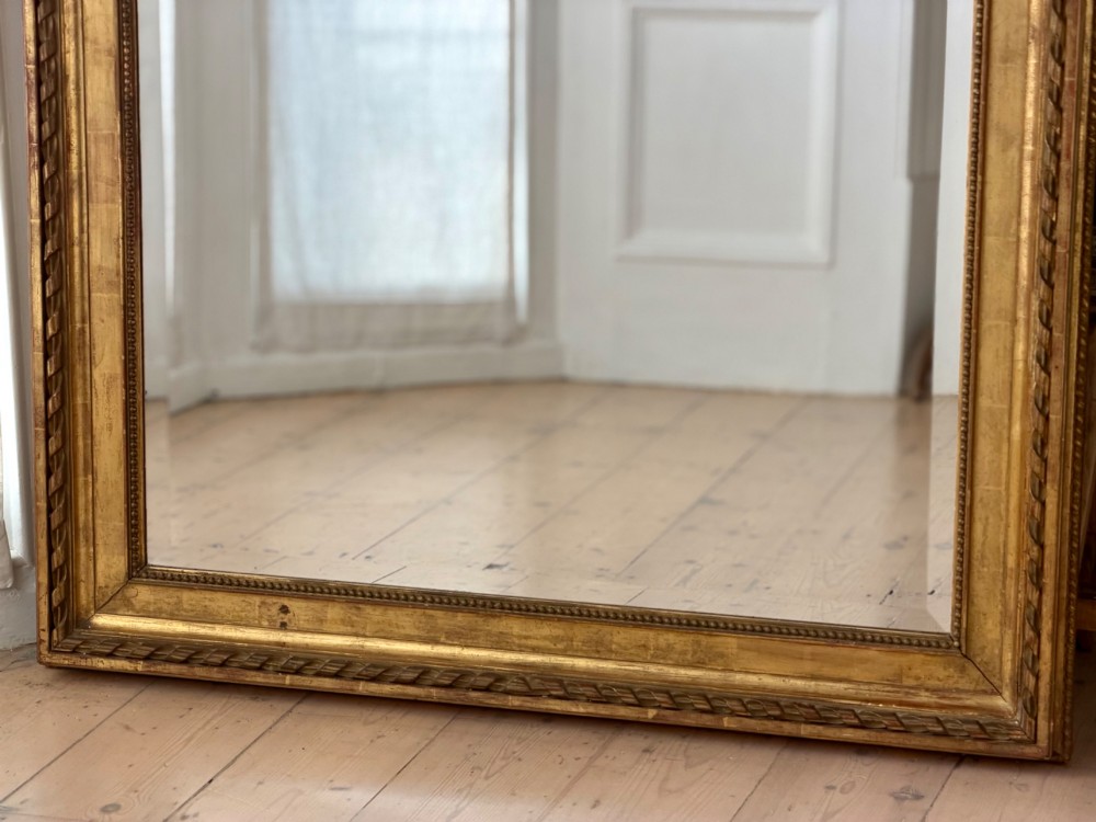A rectangular French Louis XVI style giltwood mirror featuring a carved ribbon cresting, draped floral swags, and a bevelled glass mirror plate. View IX