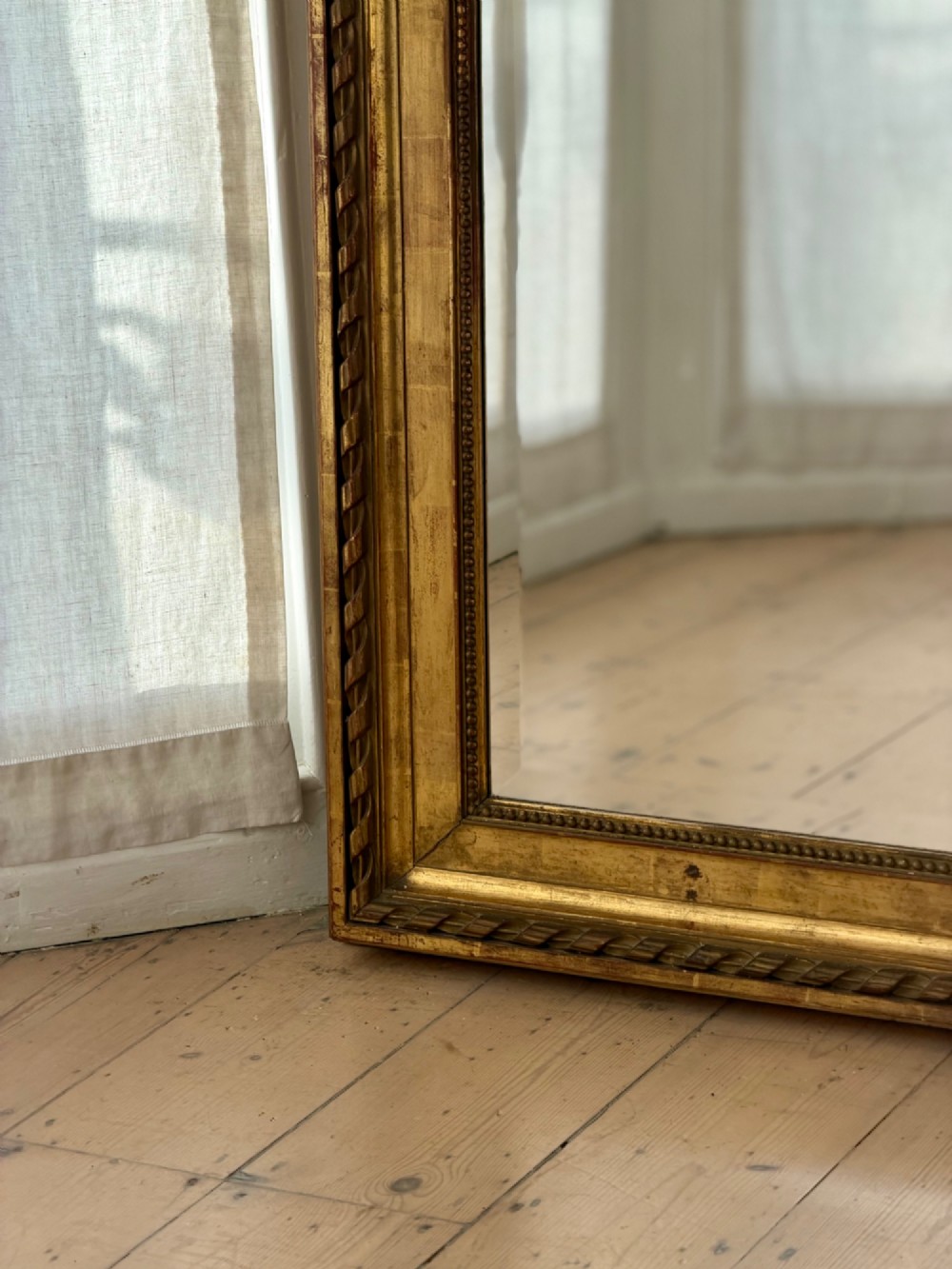A rectangular French Louis XVI style giltwood mirror featuring a carved ribbon cresting, draped floral swags, and a bevelled glass mirror plate. View X