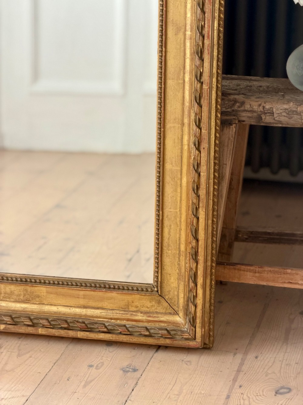 A rectangular French Louis XVI style giltwood mirror featuring a carved ribbon cresting, draped floral swags, and a bevelled glass mirror plate. View XI
