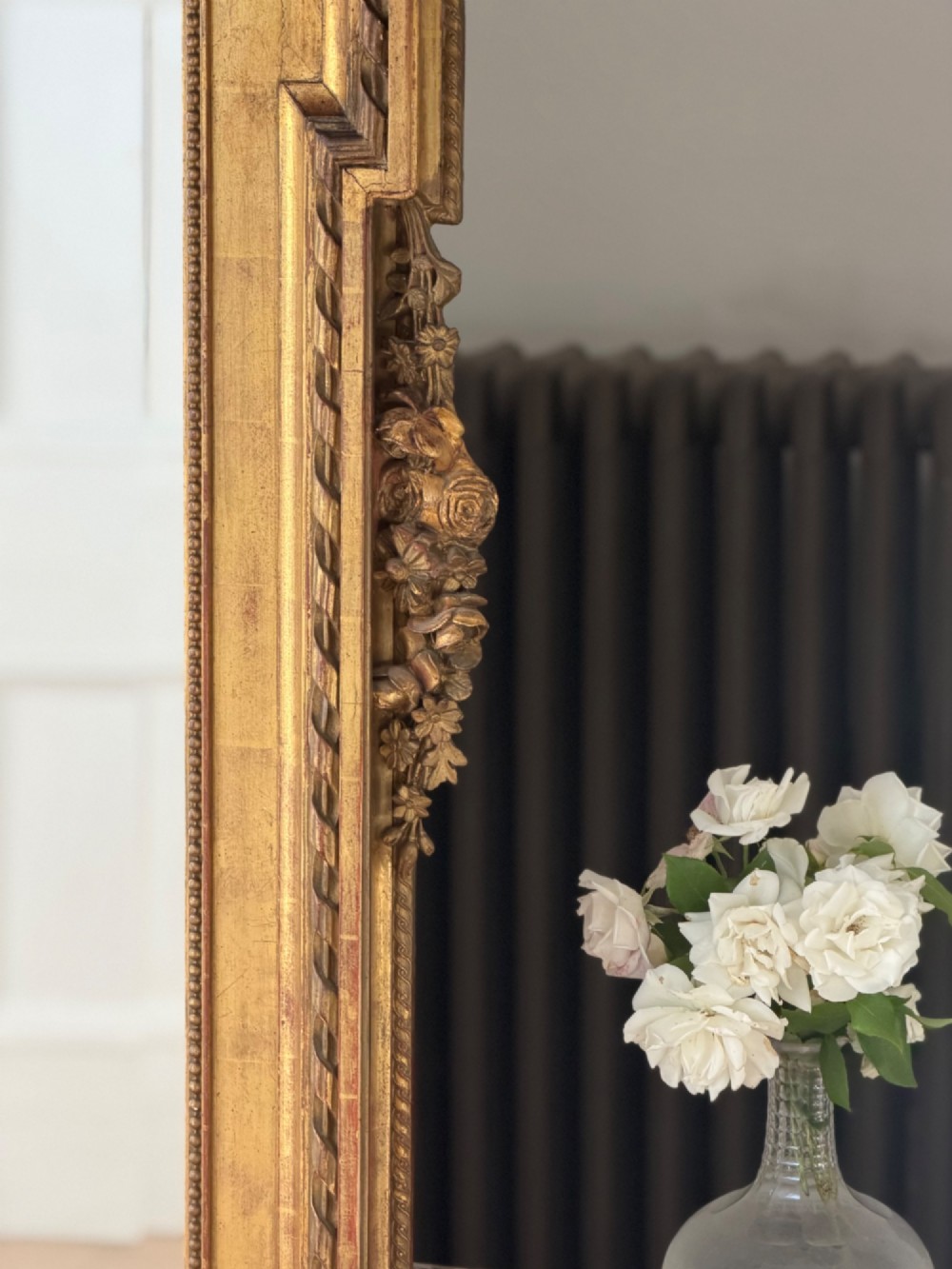 A rectangular French Louis XVI style giltwood mirror featuring a carved ribbon cresting, draped floral swags, and a bevelled glass mirror plate. View XII