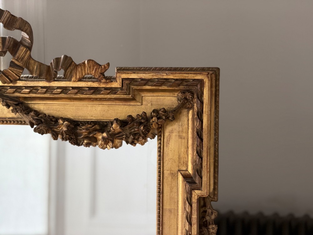 A rectangular French Louis XVI style giltwood mirror featuring a carved ribbon cresting, draped floral swags, and a bevelled glass mirror plate. View XIII