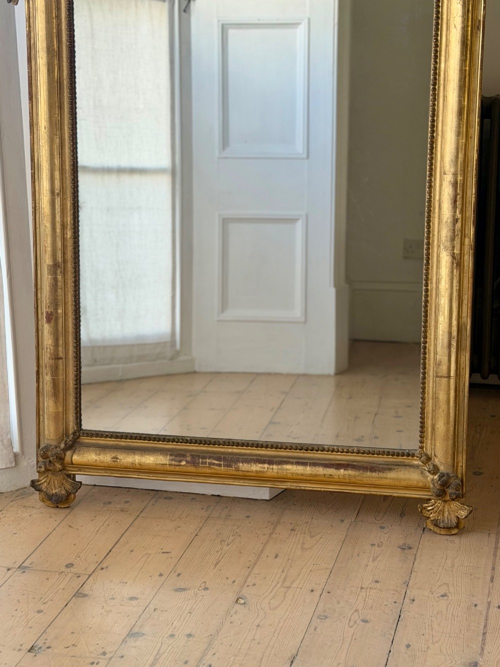 A large eighteenth-century French giltwood mirror featuring an ornate carved cresting with floral swags and a mercury glass plate. View II