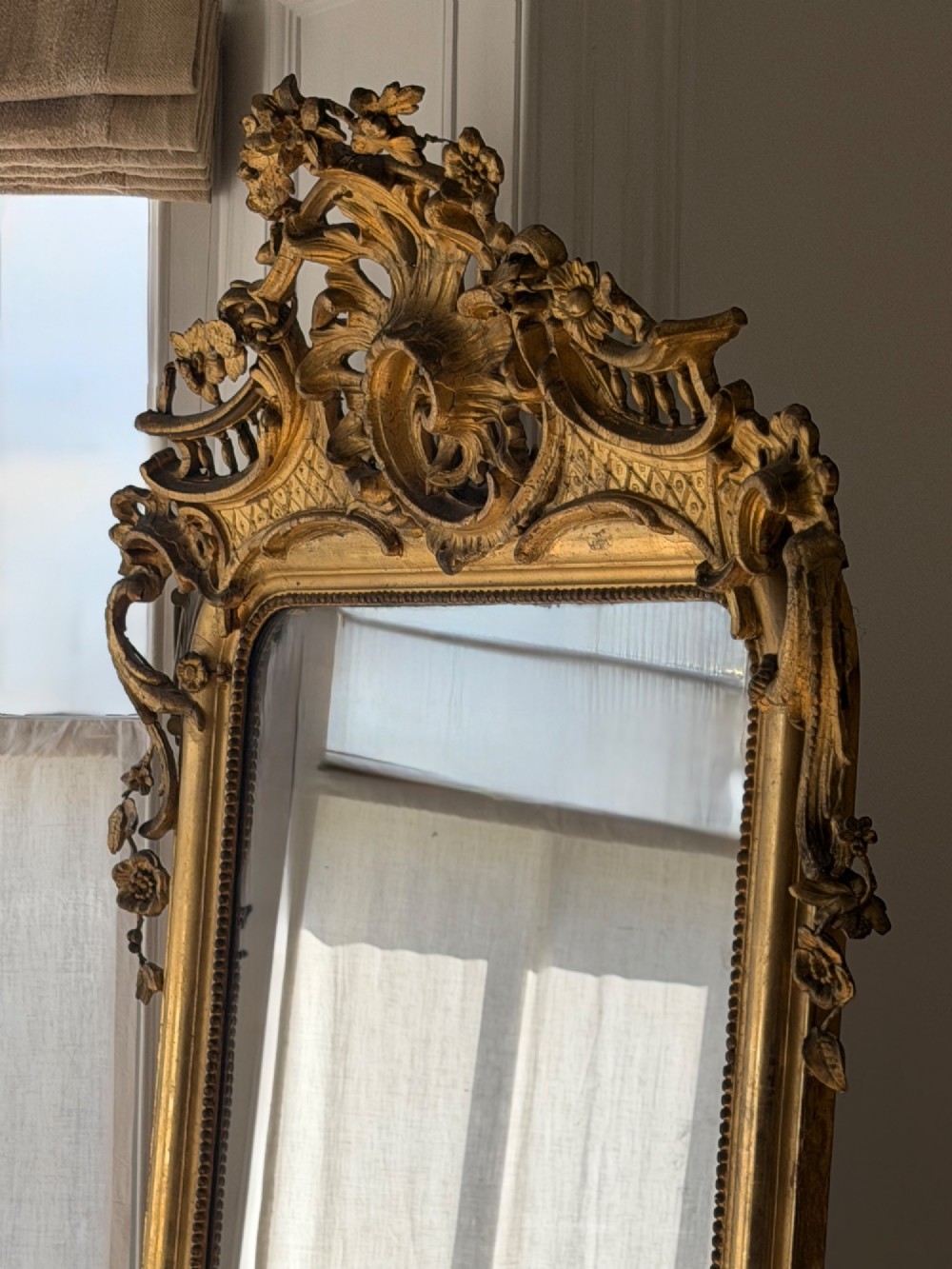 A large eighteenth-century French giltwood mirror featuring an ornate carved cresting with floral swags and a mercury glass plate. View IV