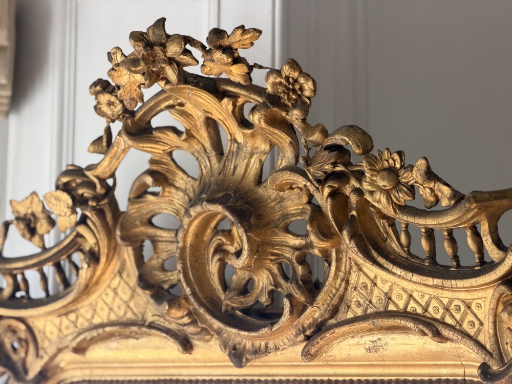 A large eighteenth-century French giltwood mirror featuring an ornate carved cresting with floral swags and a mercury glass plate. View V