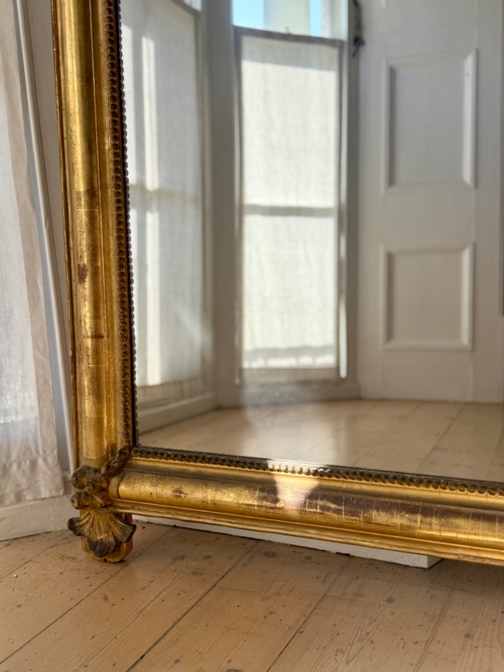 A large eighteenth-century French giltwood mirror featuring an ornate carved cresting with floral swags and a mercury glass plate. View VIII
