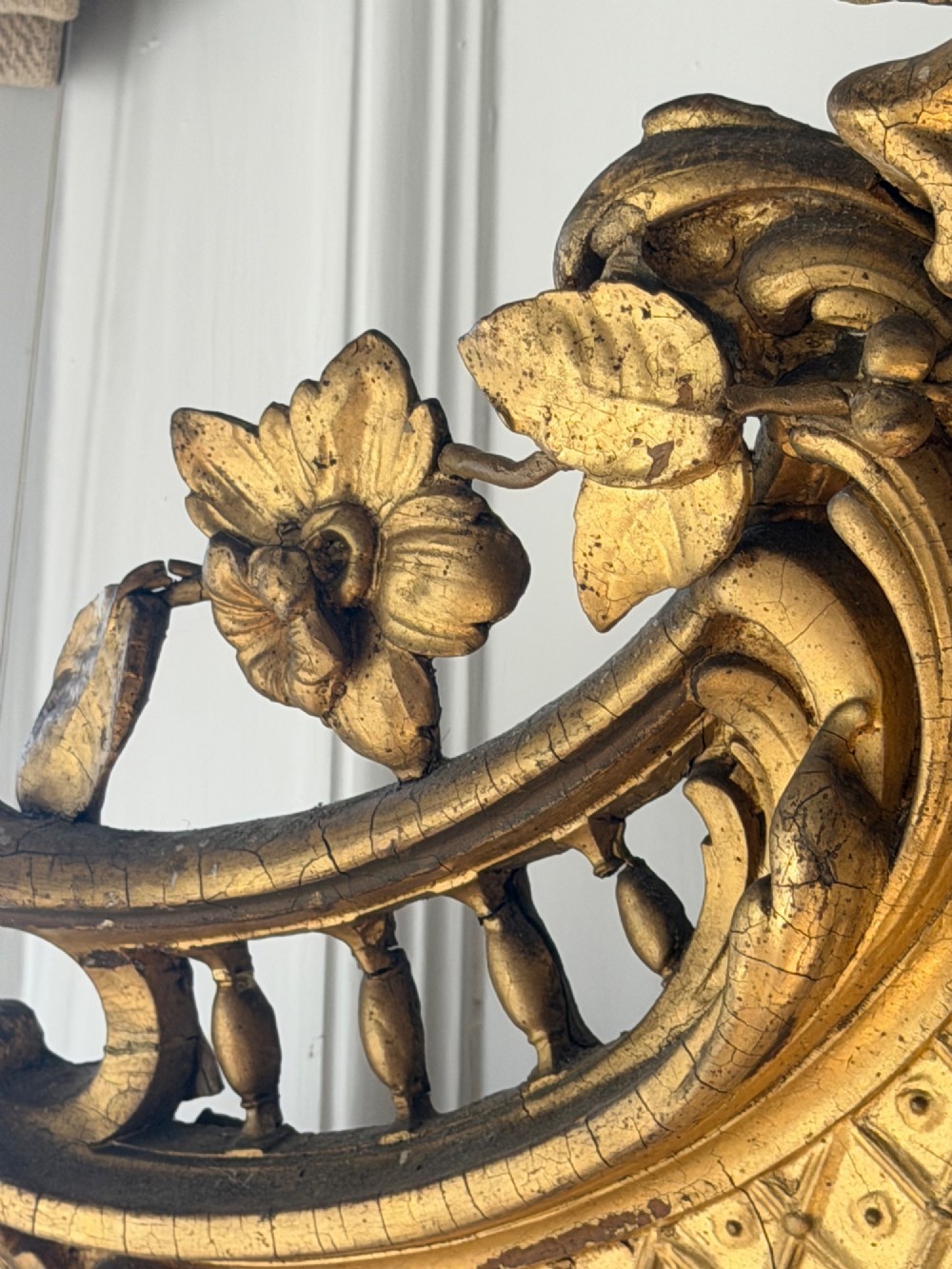 A large eighteenth-century French giltwood mirror featuring an ornate carved cresting with floral swags and a mercury glass plate. View IX