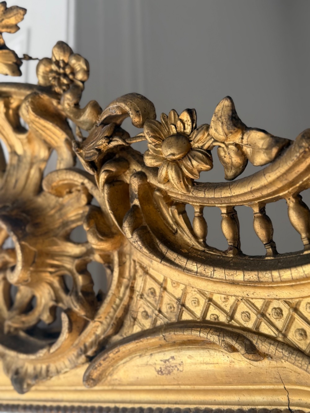 A large eighteenth-century French giltwood mirror featuring an ornate carved cresting with floral swags and a mercury glass plate. View X