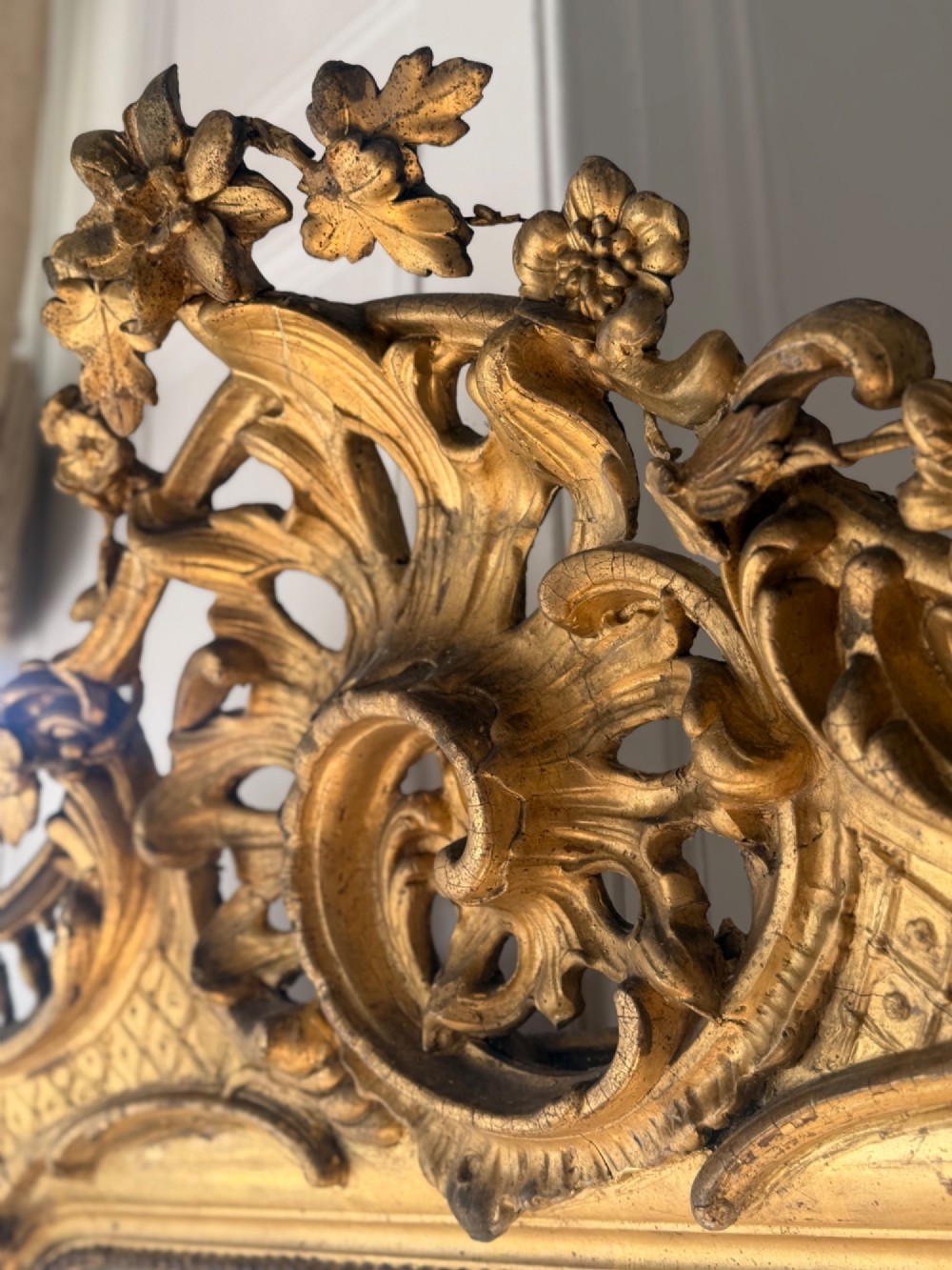 A large eighteenth-century French giltwood mirror featuring an ornate carved cresting with floral swags and a mercury glass plate. View XII