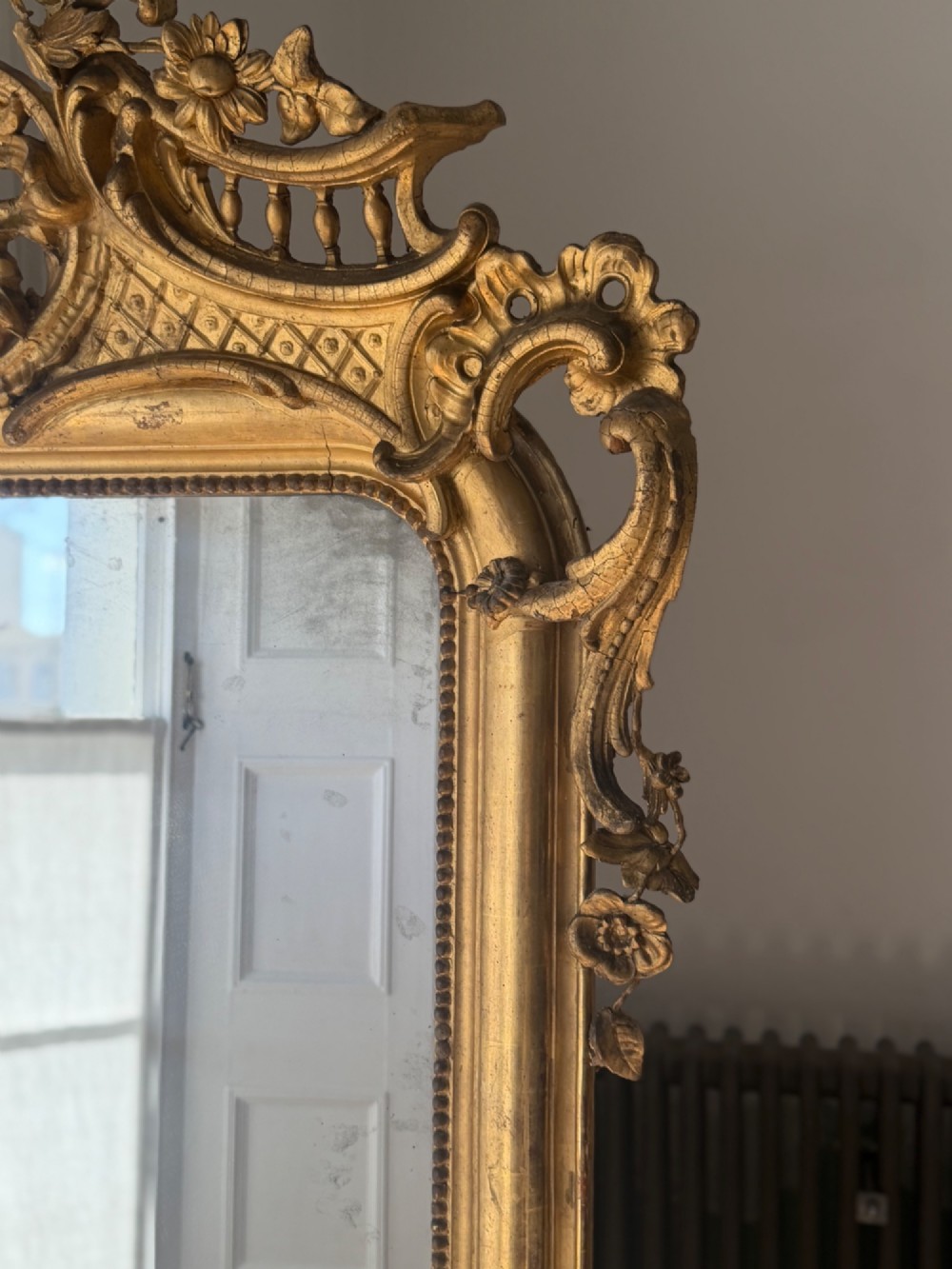A large eighteenth-century French giltwood mirror featuring an ornate carved cresting with floral swags and a mercury glass plate. View XIII