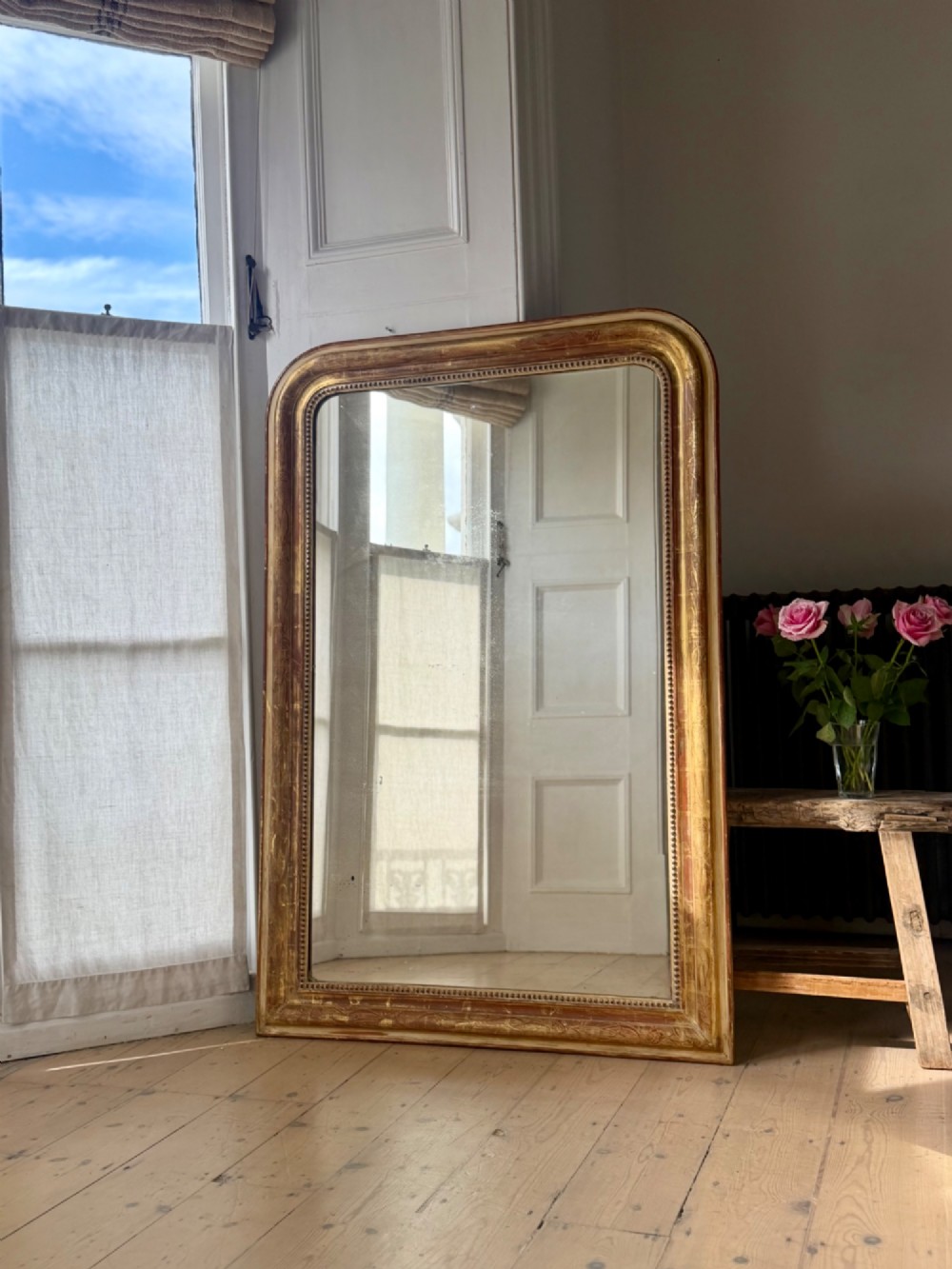 A large 19th-century French Louis Philippe giltwood mirror featuring rounded upper corners, beaded inner moulding, and visible red bole beneath aged gold leafing. View II
