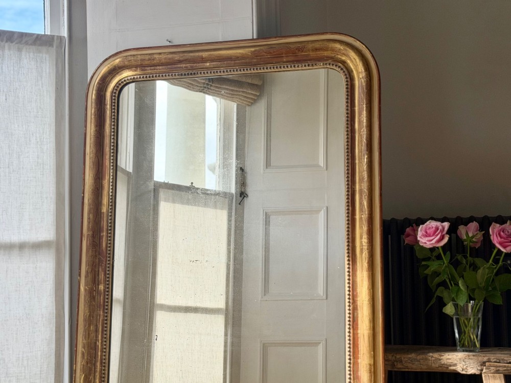 A large 19th-century French Louis Philippe giltwood mirror featuring rounded upper corners, beaded inner moulding, and visible red bole beneath aged gold leafing. View III