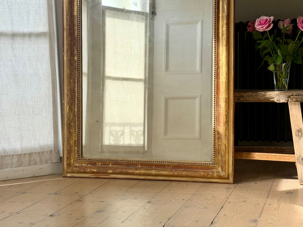 A large 19th-century French Louis Philippe giltwood mirror featuring rounded upper corners, beaded inner moulding, and visible red bole beneath aged gold leafing. View IV
