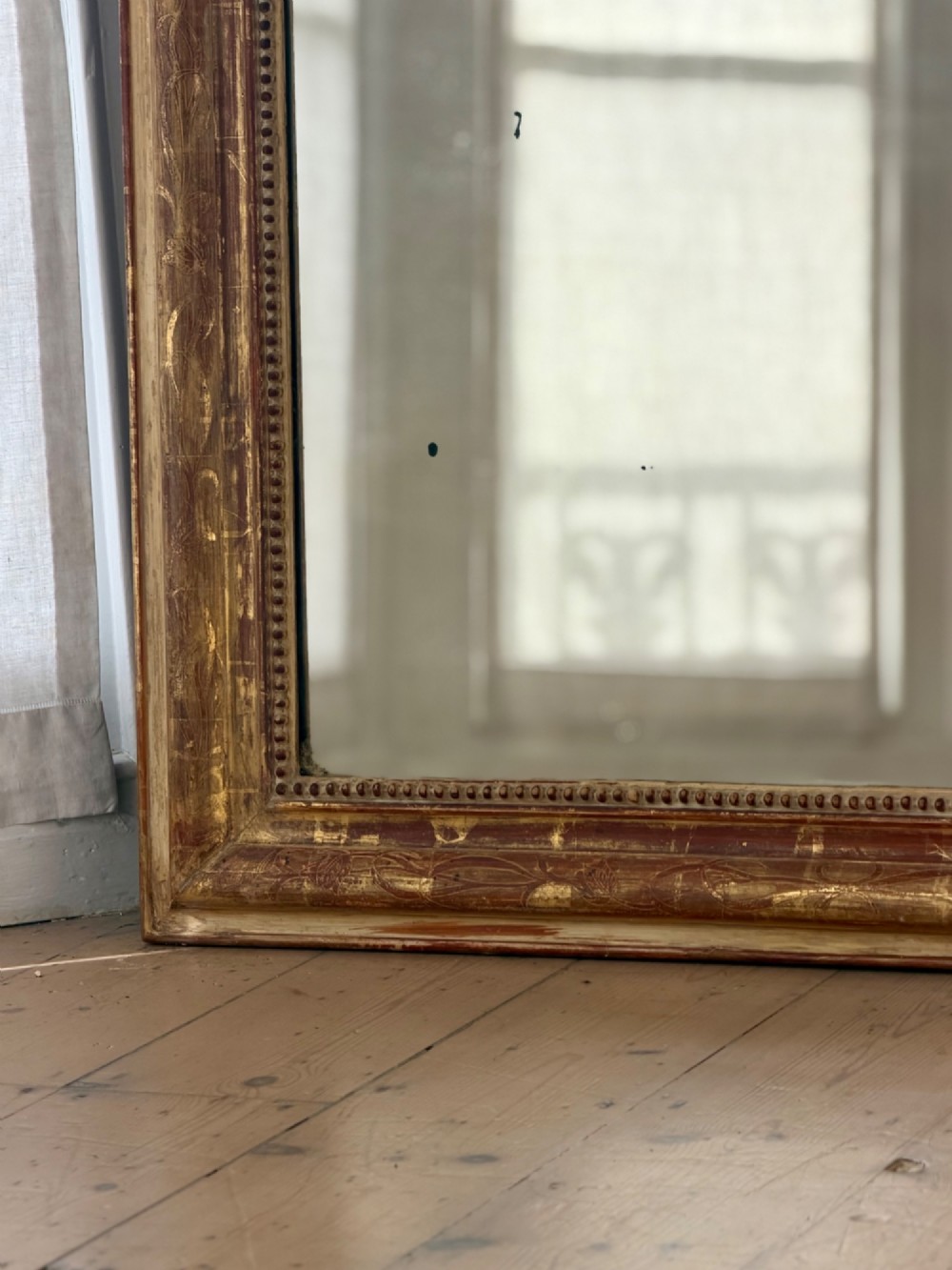 A large 19th-century French Louis Philippe giltwood mirror featuring rounded upper corners, beaded inner moulding, and visible red bole beneath aged gold leafing. View V