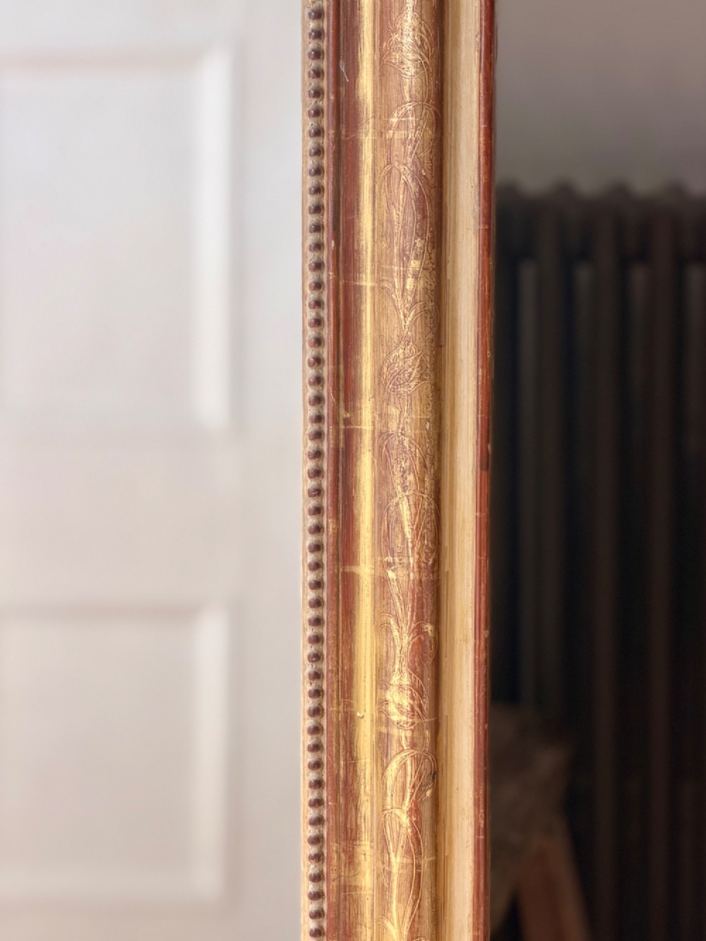 A large 19th-century French Louis Philippe giltwood mirror featuring rounded upper corners, beaded inner moulding, and visible red bole beneath aged gold leafing. View VI