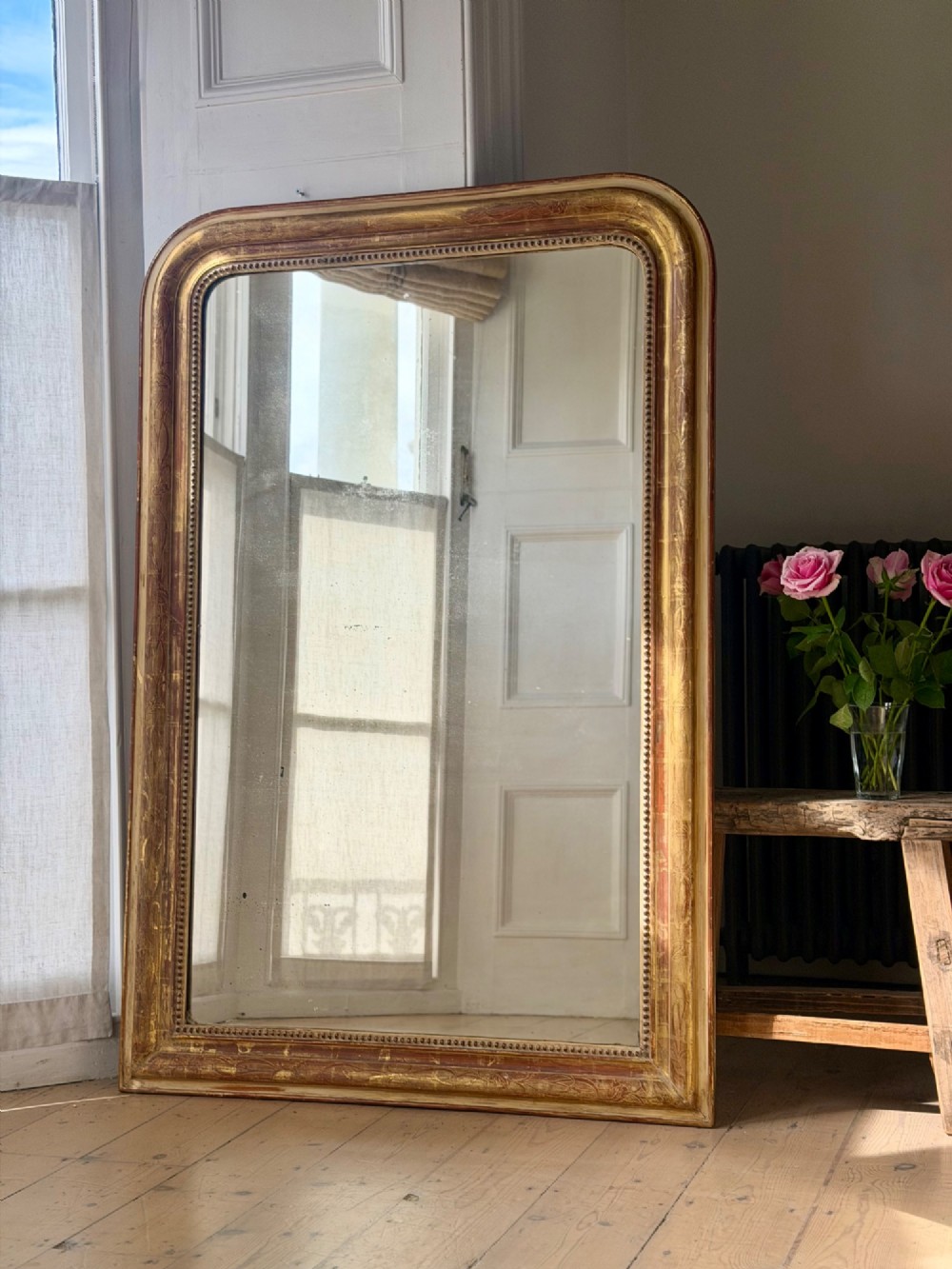 A large 19th-century French Louis Philippe giltwood mirror featuring rounded upper corners, beaded inner moulding, and visible red bole beneath aged gold leafing. View VII
