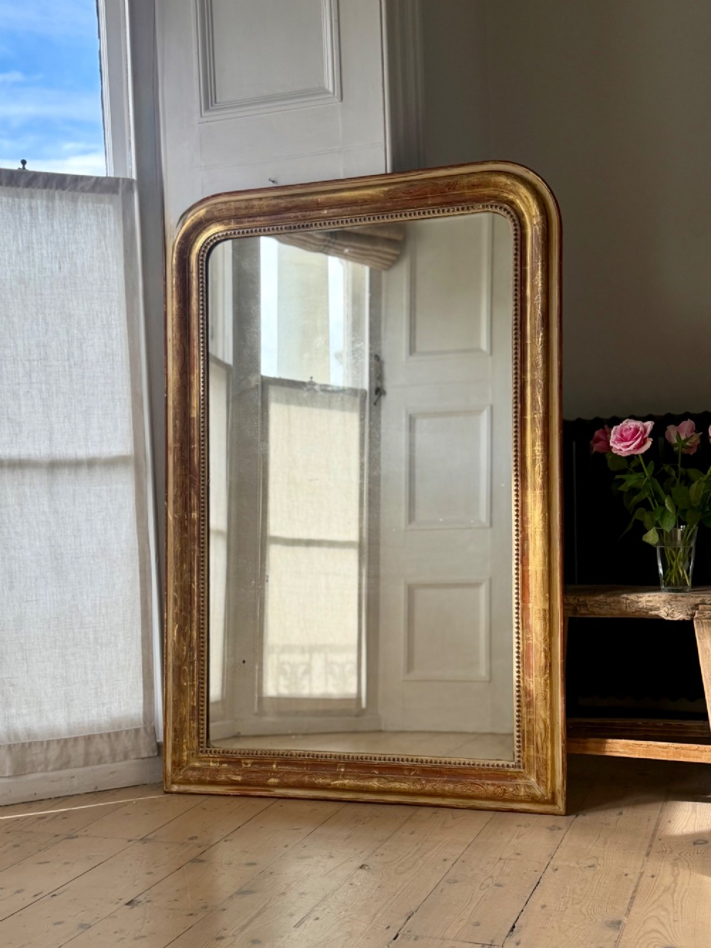 A large 19th-century French Louis Philippe giltwood mirror featuring rounded upper corners, beaded inner moulding, and visible red bole beneath aged gold leafing. View VIII