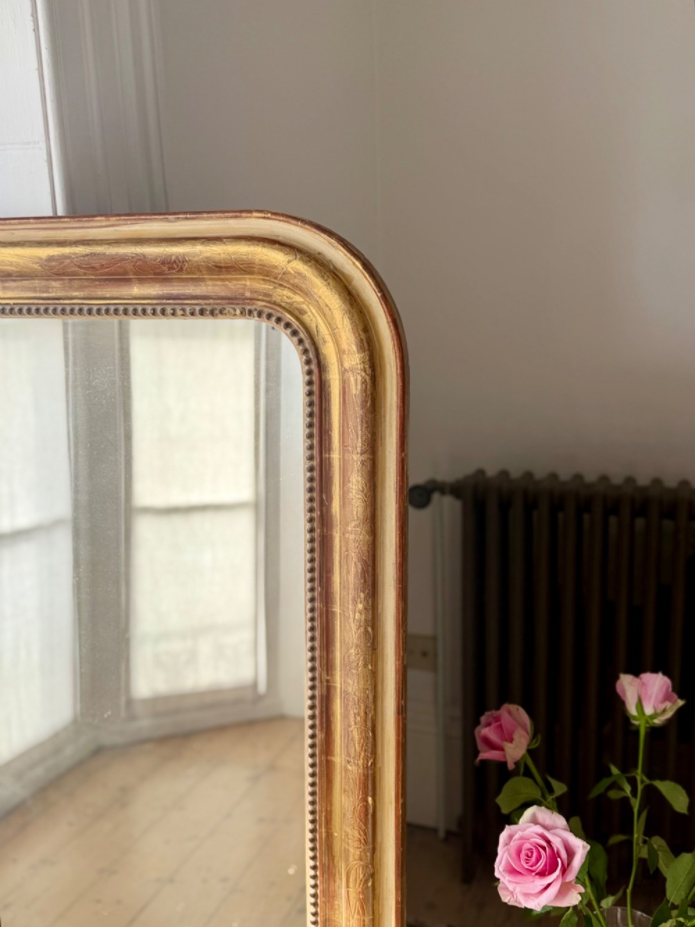 A large 19th-century French Louis Philippe giltwood mirror featuring rounded upper corners, beaded inner moulding, and visible red bole beneath aged gold leafing. View IX