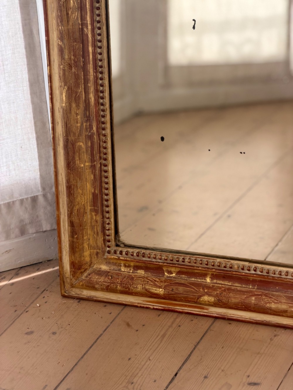 A large 19th-century French Louis Philippe giltwood mirror featuring rounded upper corners, beaded inner moulding, and visible red bole beneath aged gold leafing. View X