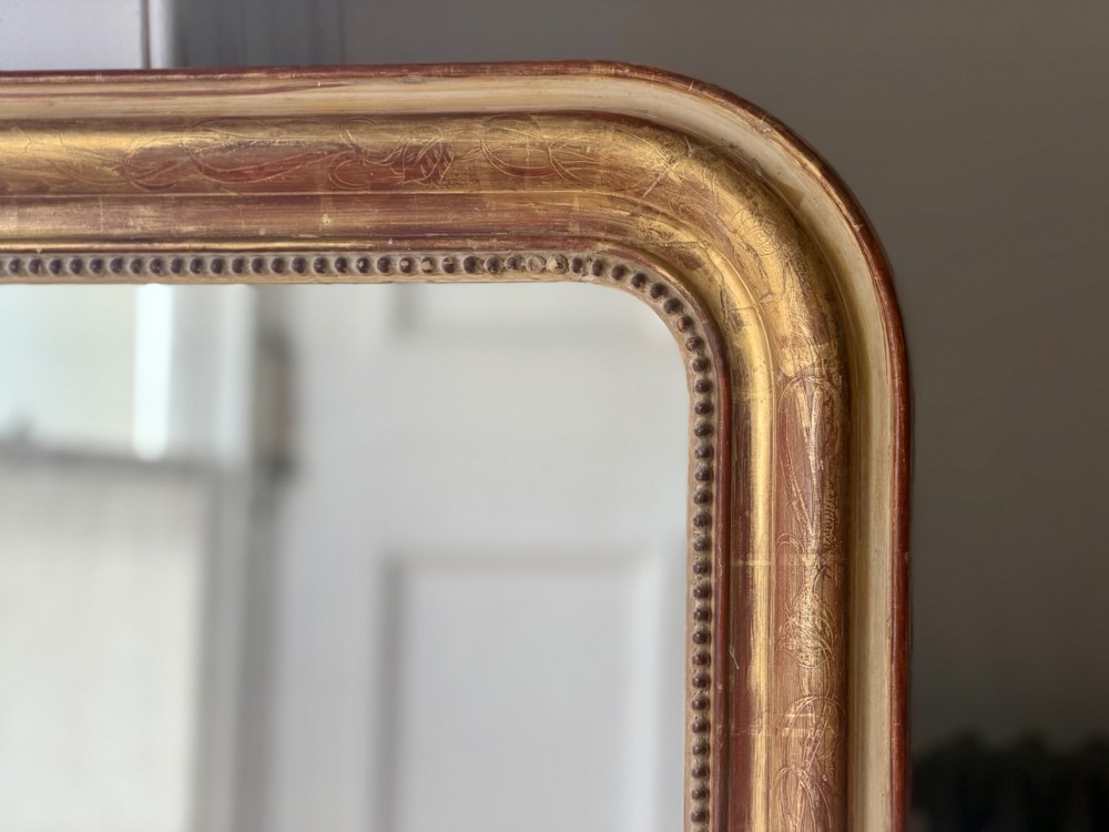 A large 19th-century French Louis Philippe giltwood mirror featuring rounded upper corners, beaded inner moulding, and visible red bole beneath aged gold leafing. View XI