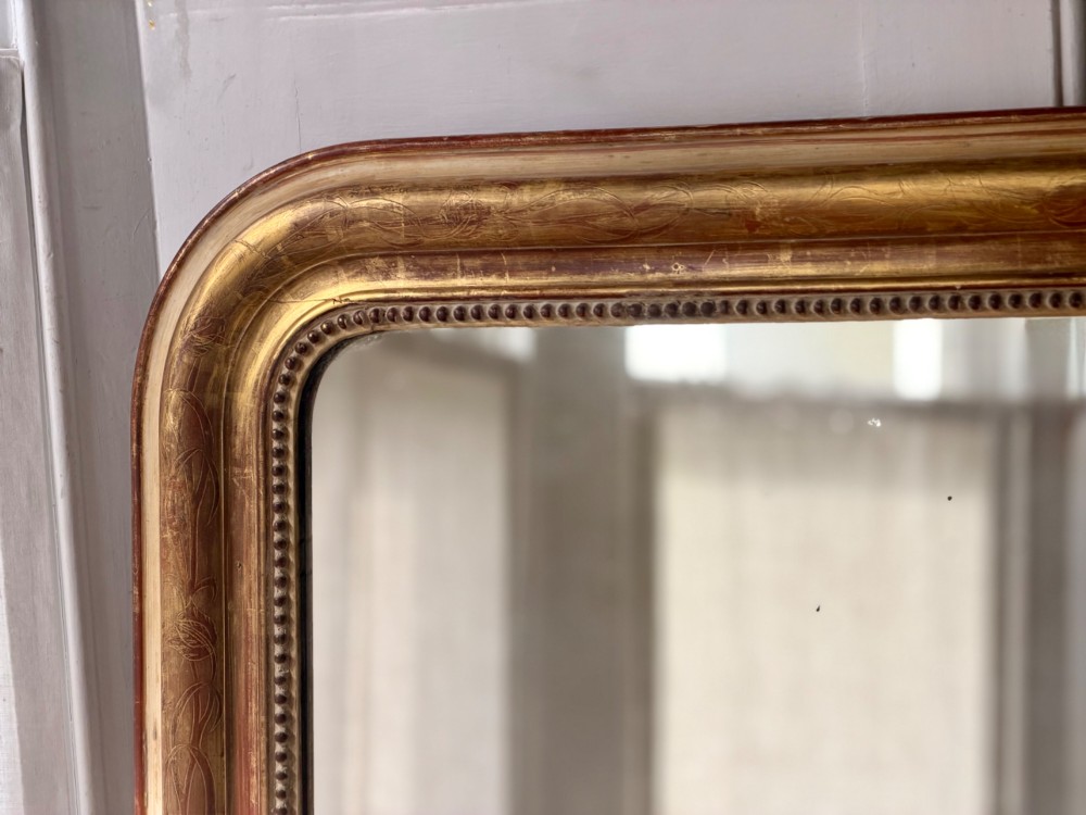 A large 19th-century French Louis Philippe giltwood mirror featuring rounded upper corners, beaded inner moulding, and visible red bole beneath aged gold leafing. View XII