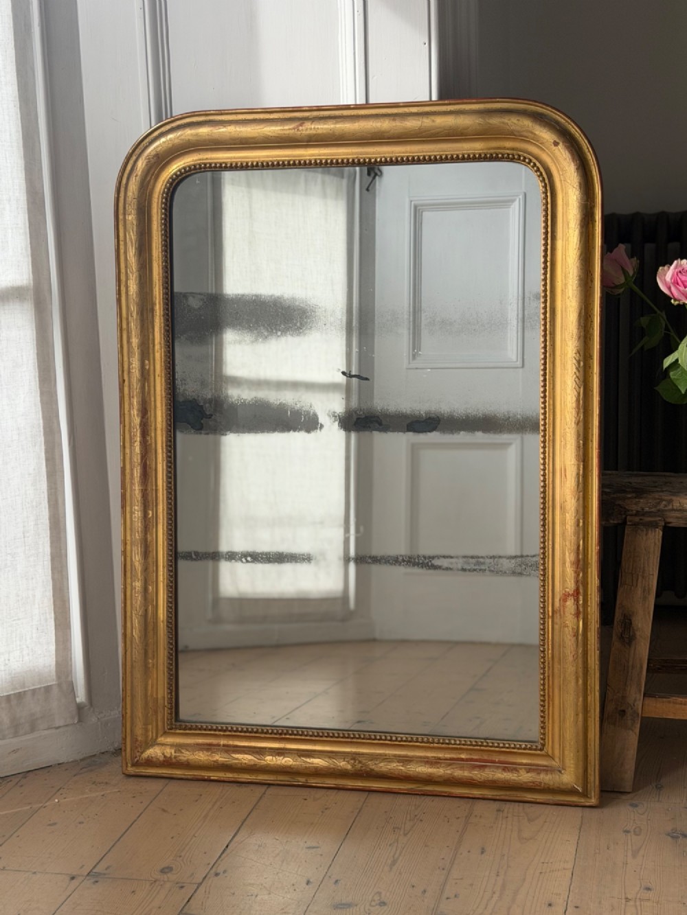 A rectangular Louis Philippe mirror featuring a rounded upper frame in gold leaf gilding with bead moulding around foxed mercury glass.