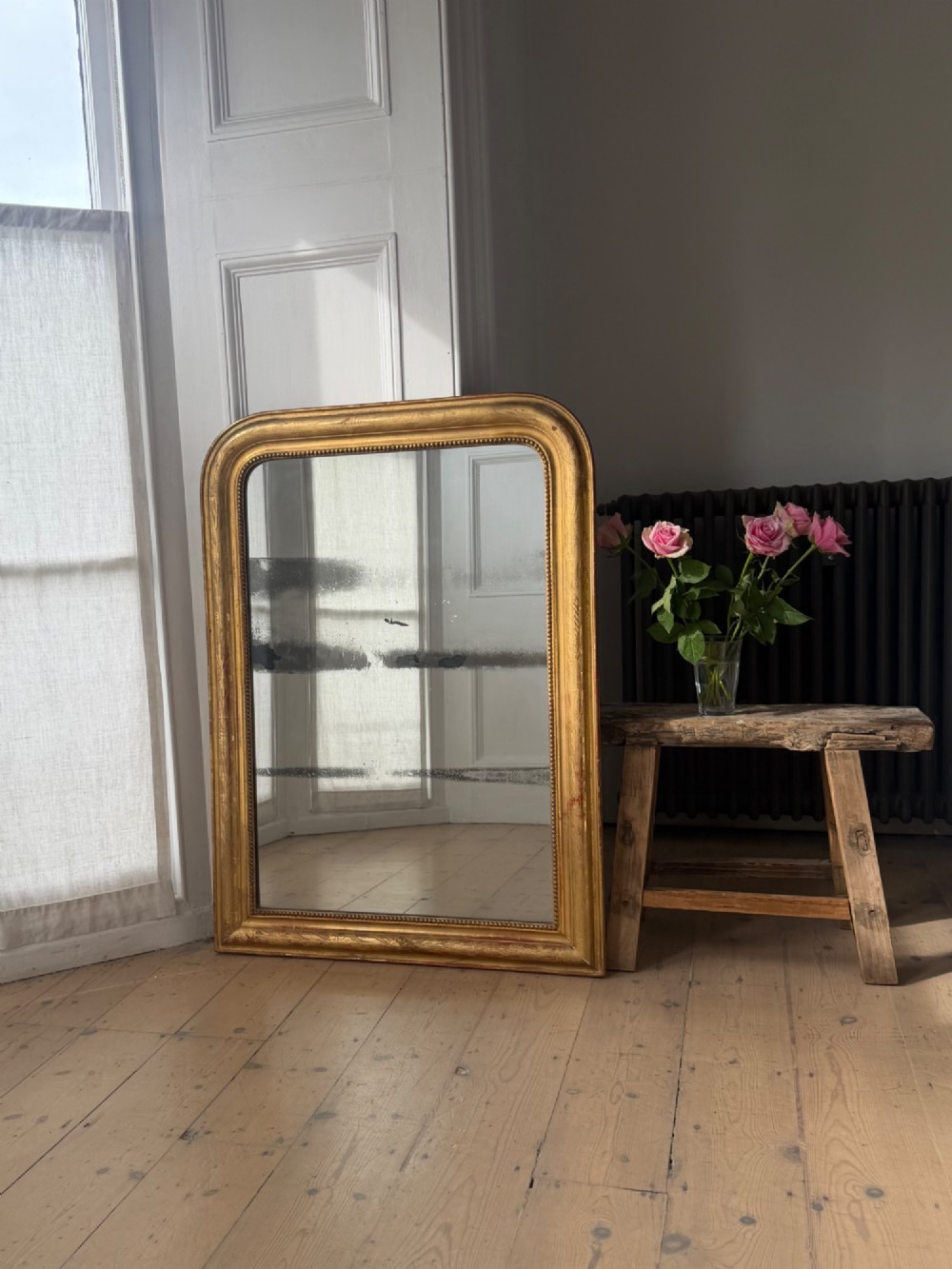 A rectangular Louis Philippe mirror featuring a rounded upper frame in gold leaf gilding with bead moulding around foxed mercury glass. View II