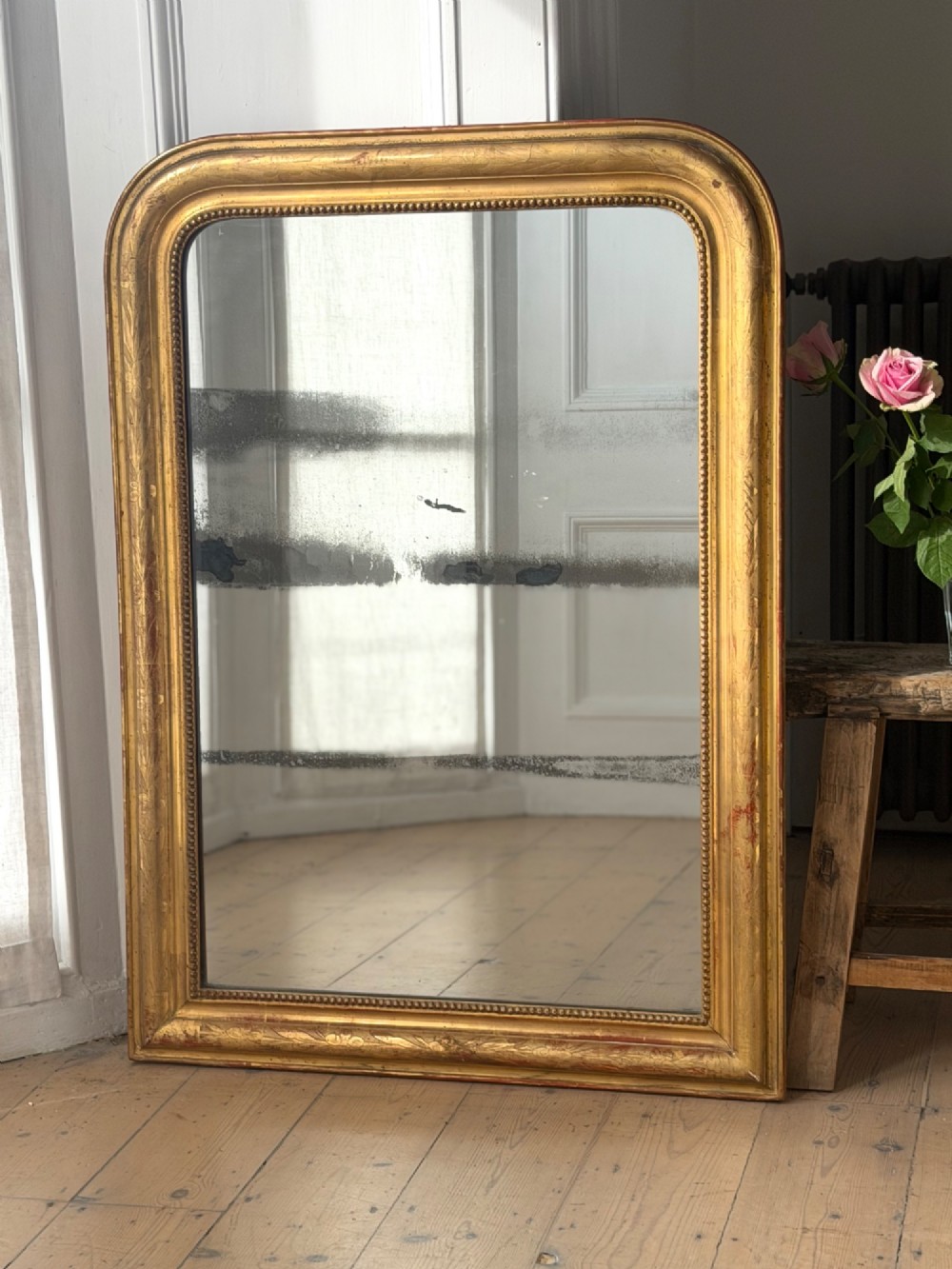 A rectangular Louis Philippe mirror featuring a rounded upper frame in gold leaf gilding with bead moulding around foxed mercury glass. View IV
