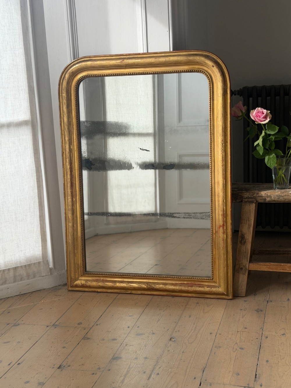 A rectangular Louis Philippe mirror featuring a rounded upper frame in gold leaf gilding with bead moulding around foxed mercury glass. View V