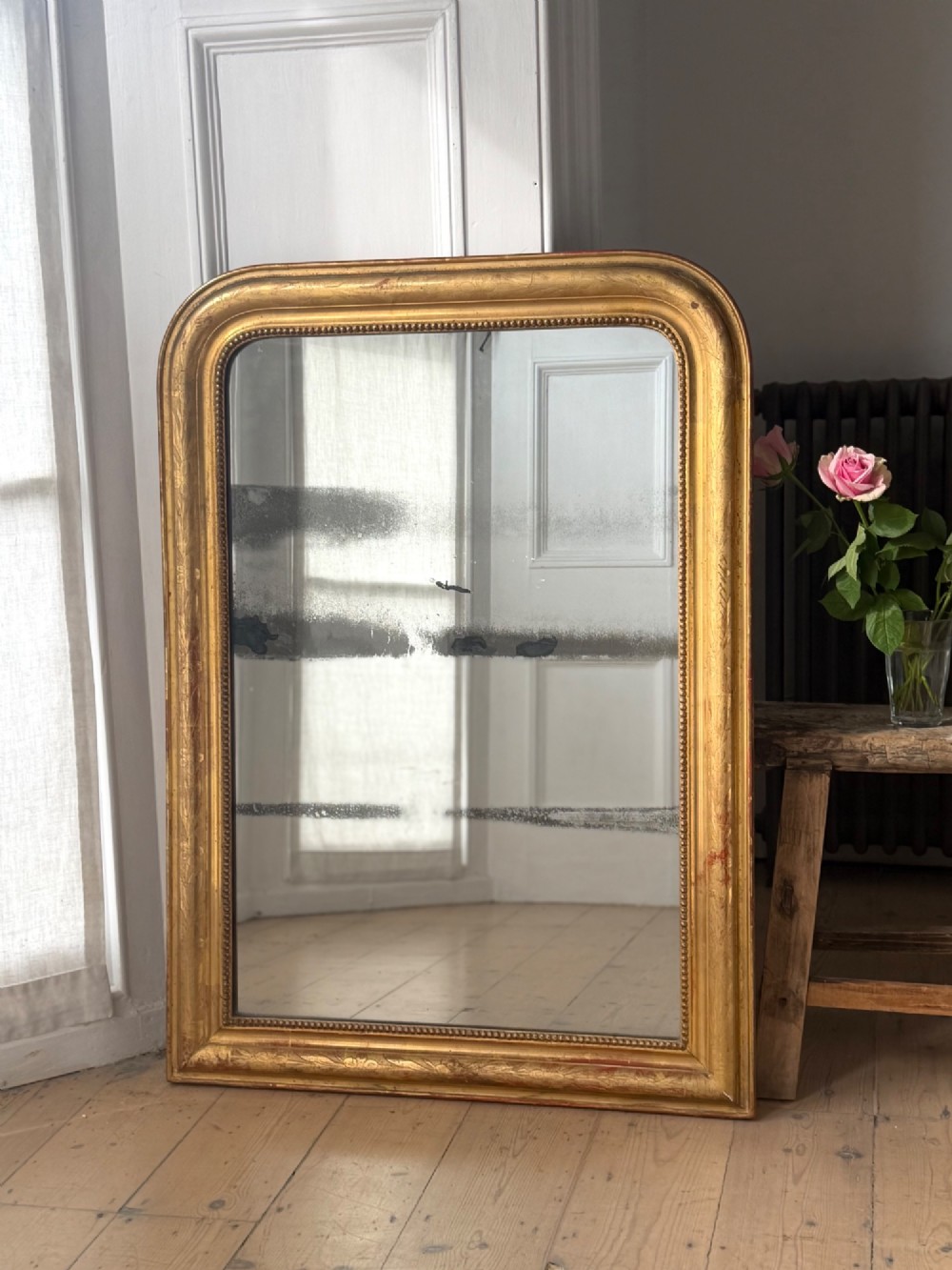 A rectangular Louis Philippe mirror featuring a rounded upper frame in gold leaf gilding with bead moulding around foxed mercury glass. View VII