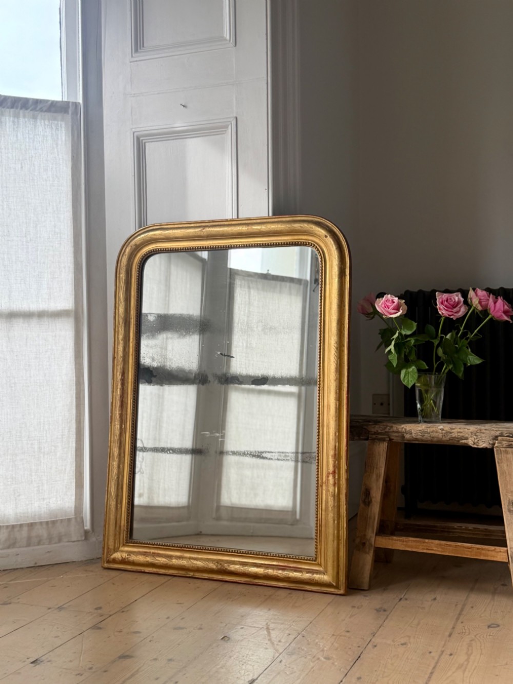 A rectangular Louis Philippe mirror featuring a rounded upper frame in gold leaf gilding with bead moulding around foxed mercury glass. View VIII