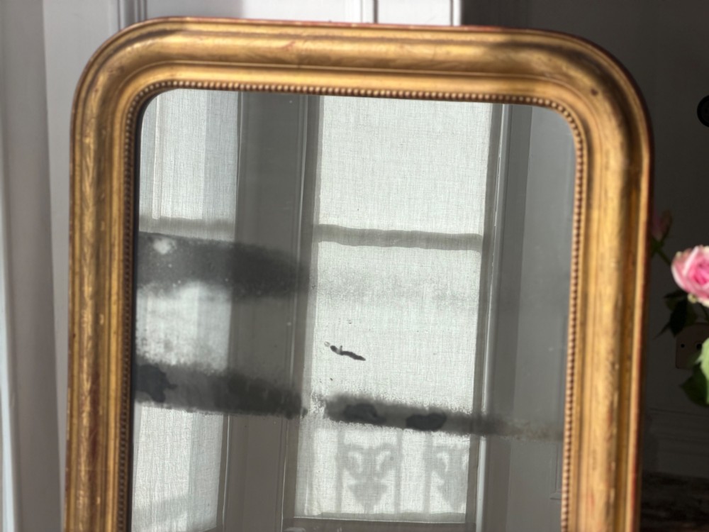 A rectangular Louis Philippe mirror featuring a rounded upper frame in gold leaf gilding with bead moulding around foxed mercury glass. View IX