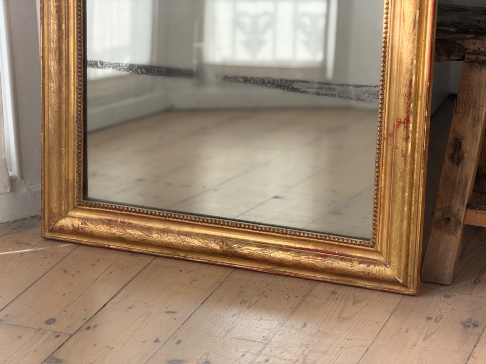 A rectangular Louis Philippe mirror featuring a rounded upper frame in gold leaf gilding with bead moulding around foxed mercury glass. View X