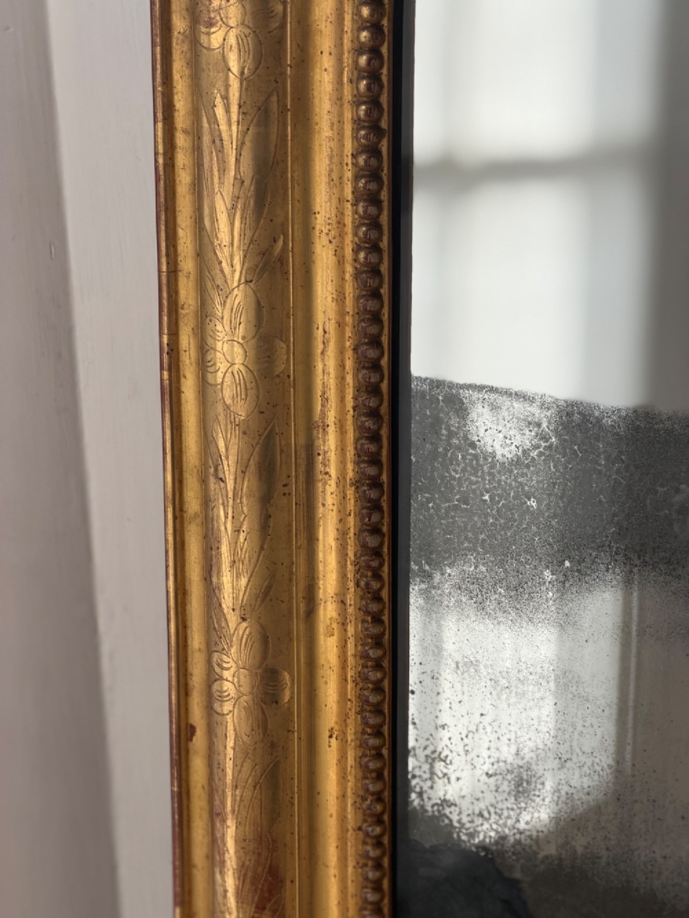 A rectangular Louis Philippe mirror featuring a rounded upper frame in gold leaf gilding with bead moulding around foxed mercury glass. View XII