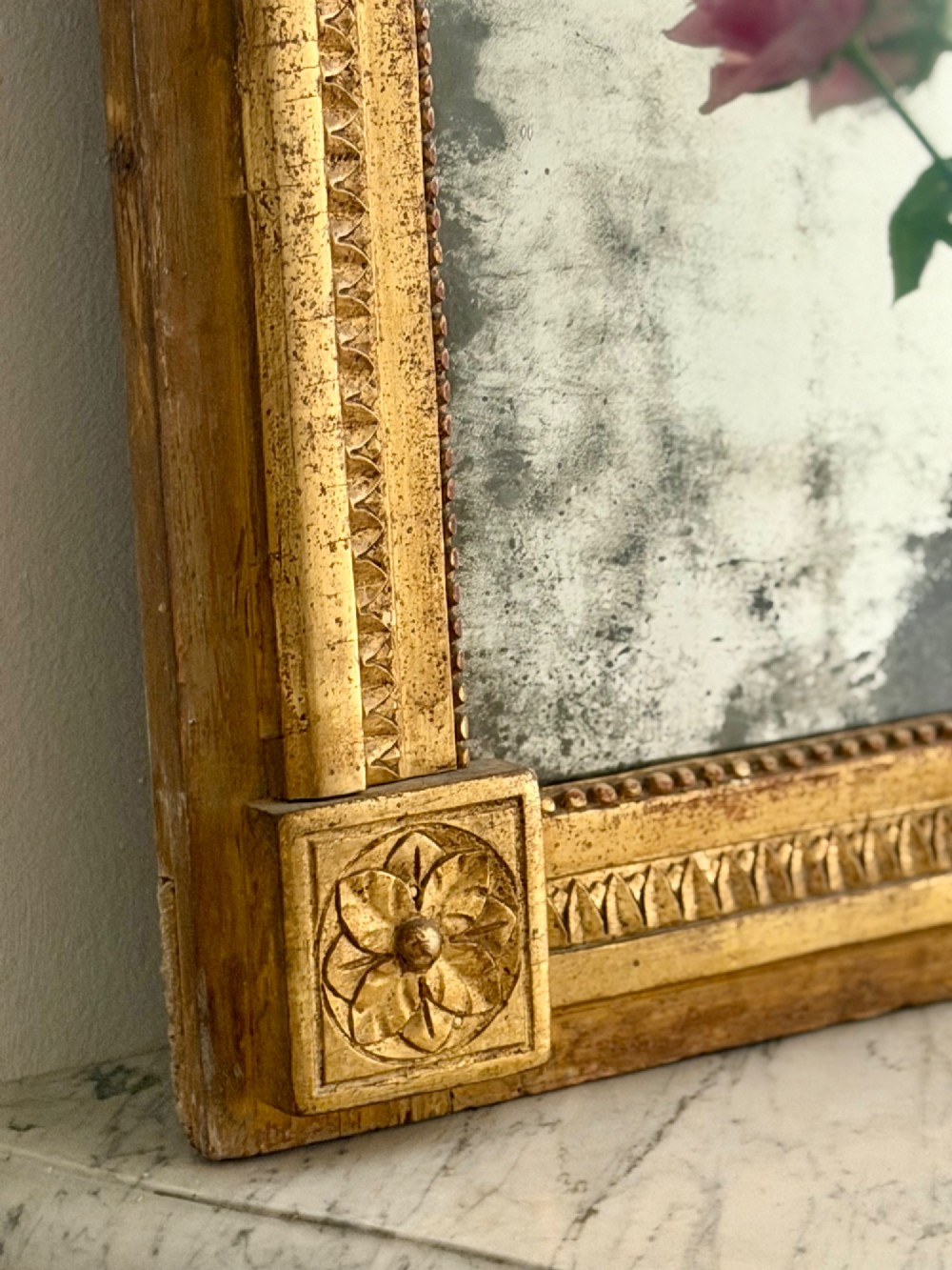 A rectangular 18th-century French giltwood mirror featuring heavy foxing on the glass plate and carved corner rosette details. View IV