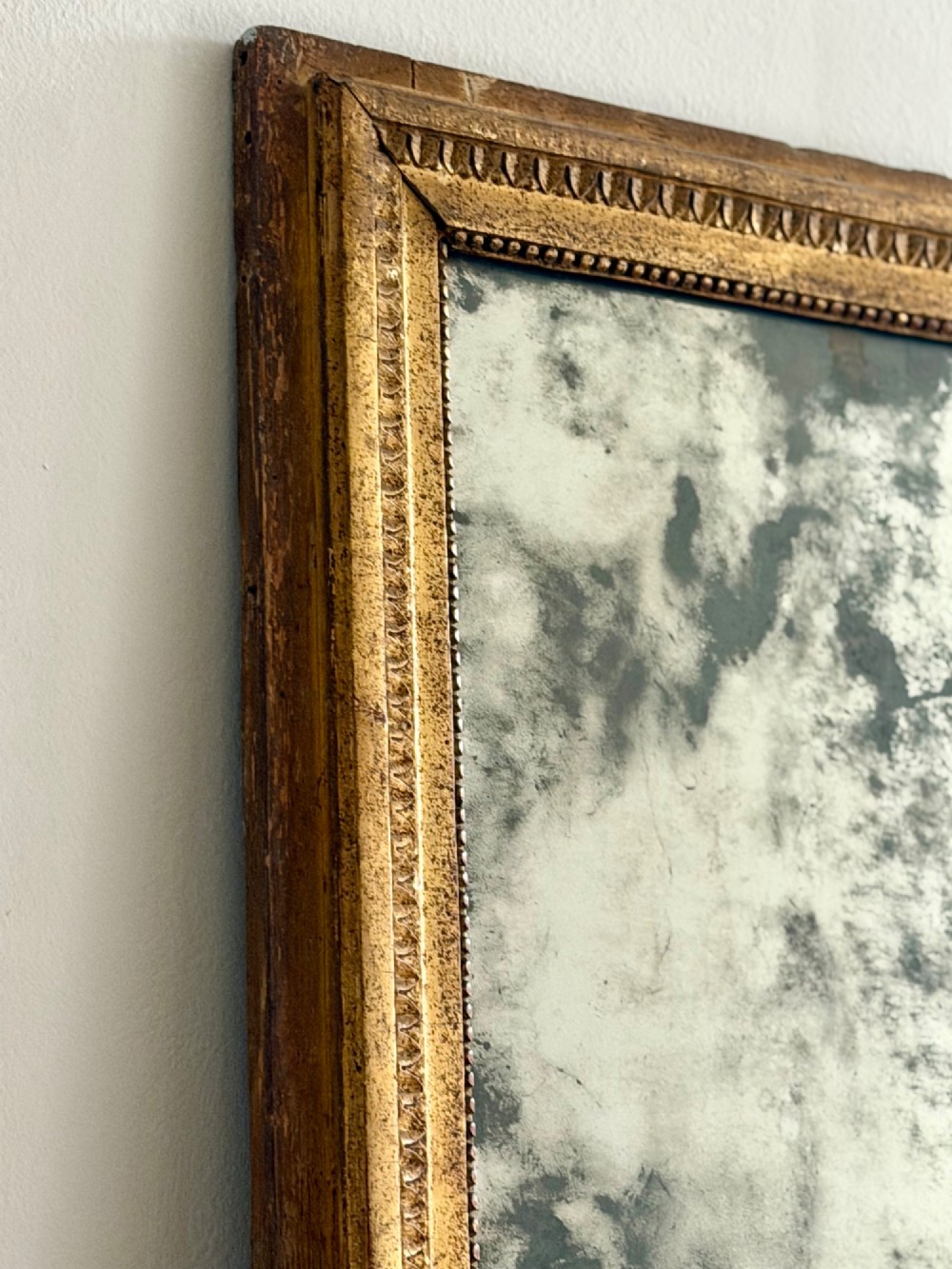 A rectangular 18th-century French giltwood mirror featuring heavy foxing on the glass plate and carved corner rosette details. View VII