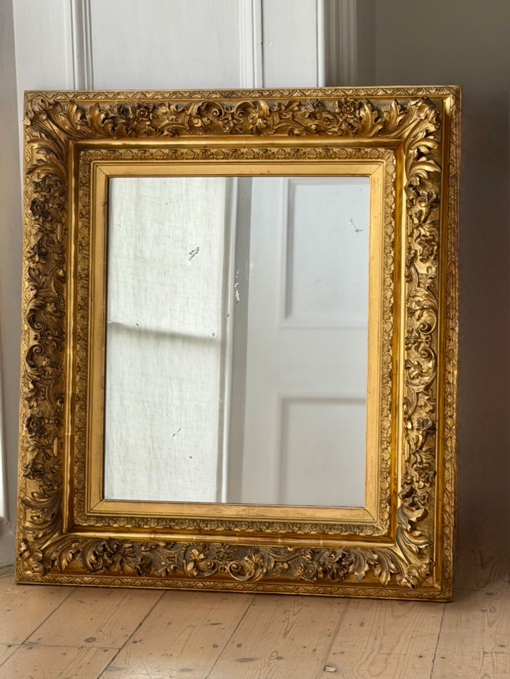 An antique rectangular French mirror featuring a carved giltwood frame with detailed leaf moulding and a mercury glass plate showing light foxing.