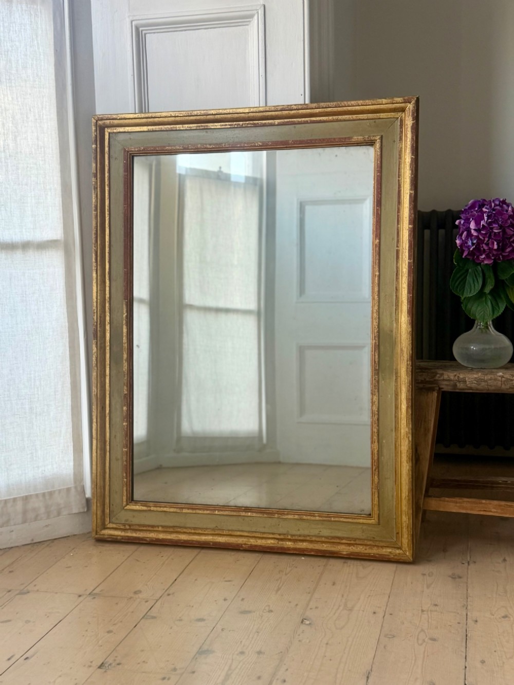 A large rectangular antique French mirror with a gold leaf and sage green painted wooden frame housing an original mercury glass plate.