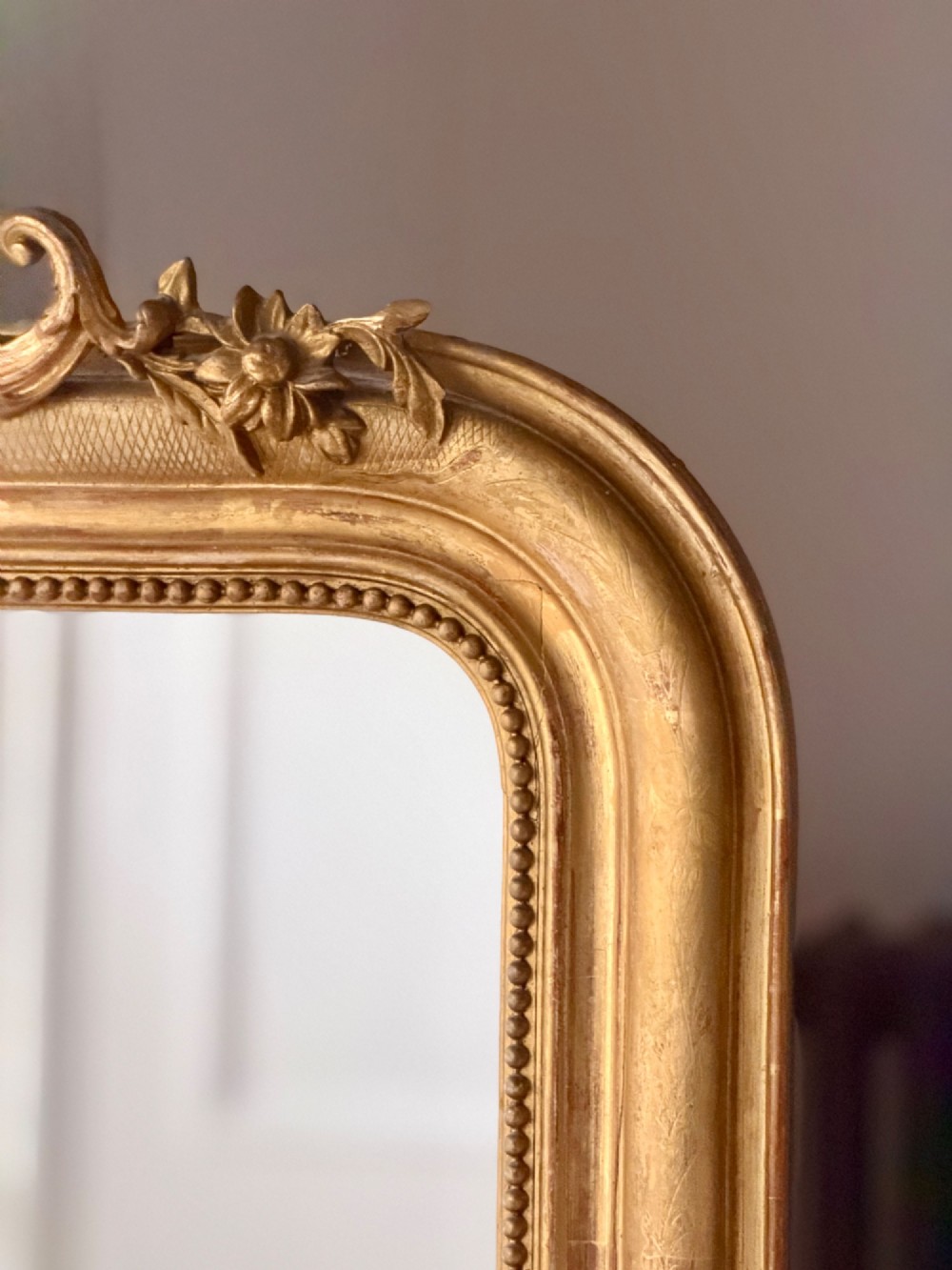 A tall French Louis Philippe mirror featuring a gold leaf frame with rounded upper shoulders, pearl bead moulding, and a decorative carved crest. View II