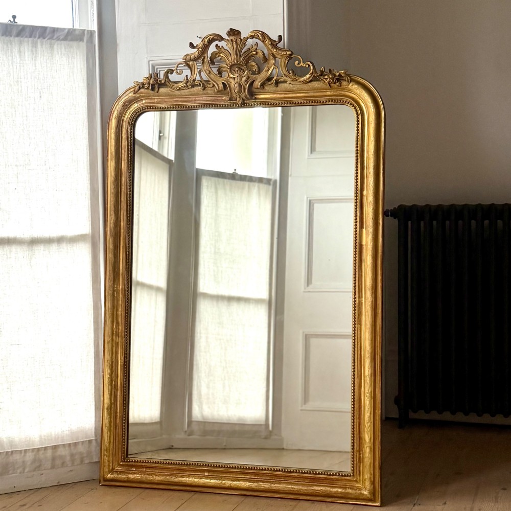A tall French Louis Philippe mirror featuring a gold leaf frame with rounded upper shoulders, pearl bead moulding, and a decorative carved crest. View IV