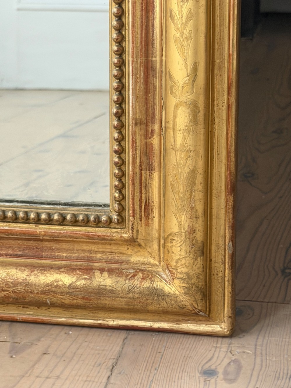 A tall French Louis Philippe mirror featuring a gold leaf frame with rounded upper shoulders, pearl bead moulding, and a decorative carved crest. View VI