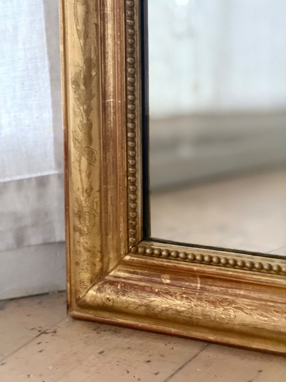 A tall French Louis Philippe mirror featuring a gold leaf frame with rounded upper shoulders, pearl bead moulding, and a decorative carved crest. View VII