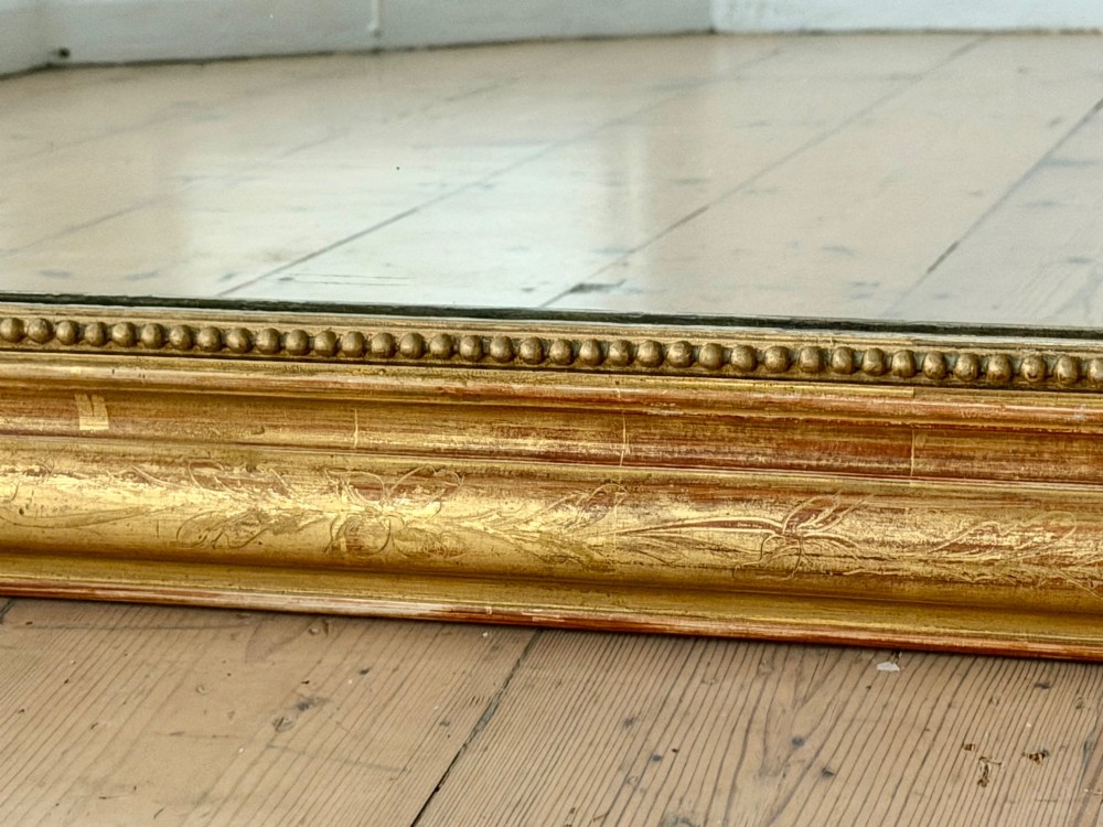 A tall French Louis Philippe mirror featuring a gold leaf frame with rounded upper shoulders, pearl bead moulding, and a decorative carved crest. View IX
