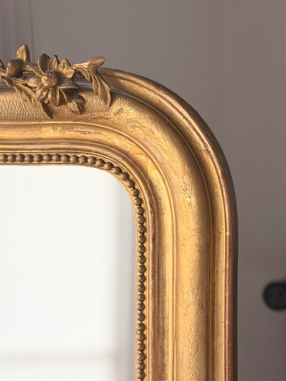 A tall French Louis Philippe mirror featuring a gold leaf frame with rounded upper shoulders, pearl bead moulding, and a decorative carved crest. View X